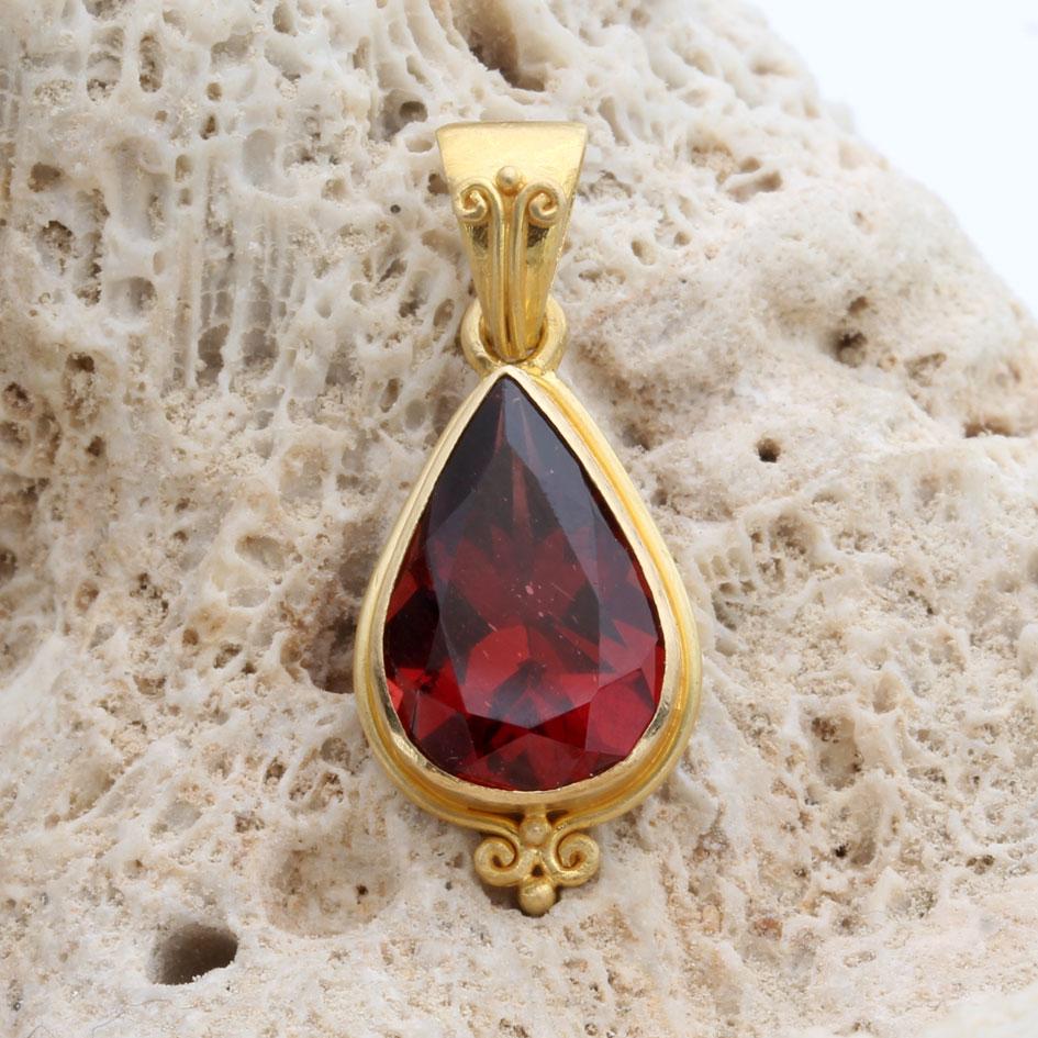 A bright red 8 x 12 mm pear shaped faceted Mozambique garnet is held in a signature artisan crafted 