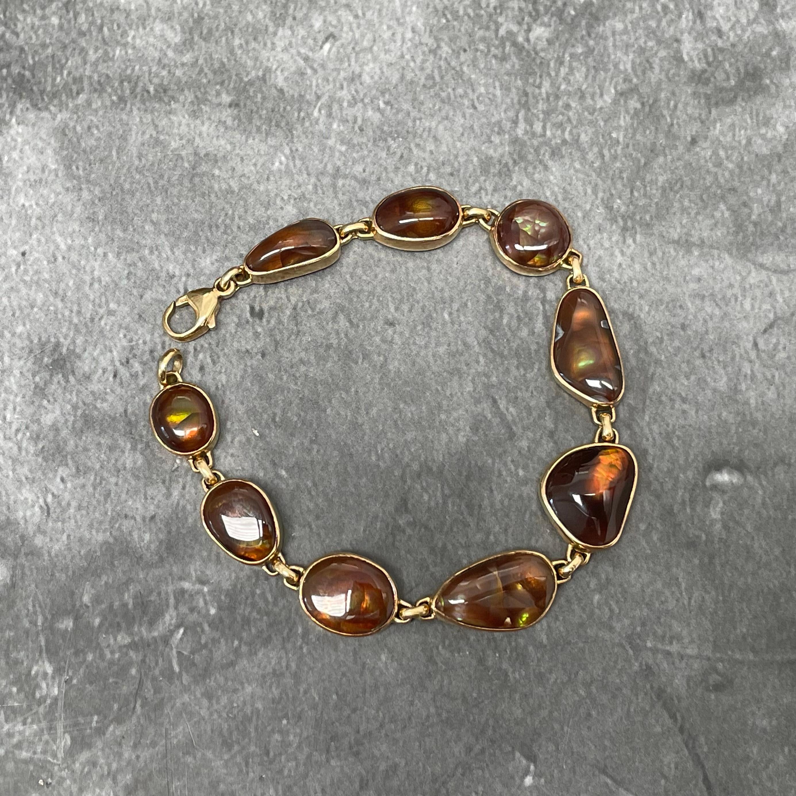 Nine irregular Arizona fire agate cabochons approximately 7 x 10 to 11 x 15 mm in size flash in iridescent greens, oranges, reds, and gold in this beautiful handmade 18K gold bracelet.  The vibrant iridescent rainbow colors found within fire agates,