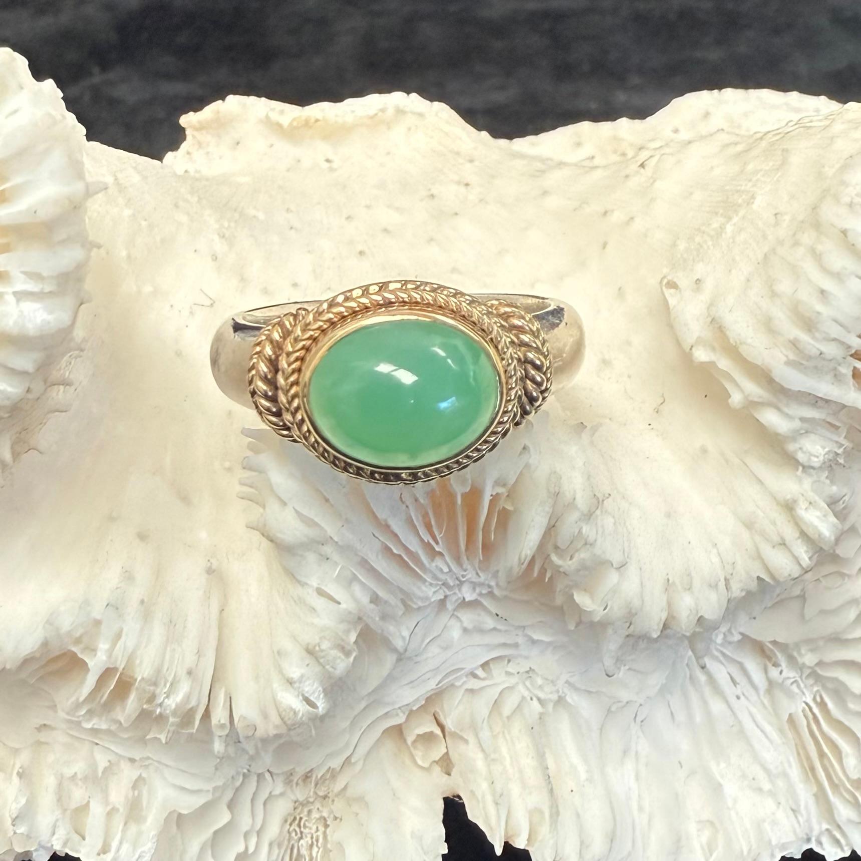 Un luminoso cabochon di crisoprasio australiano verde lime di 8 x 10 mm poggia orizzontalmente in un lussuoso abbraccio di 