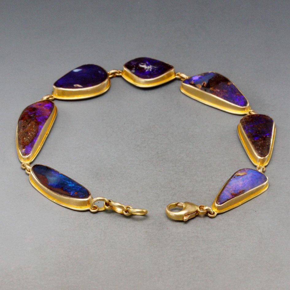Seven irregular cut cabochons of shimmering blueish and purplish Australian boulder opal from the Quilpie region in Queensland are set in simple matte-finish 18K gold bezels with  surrounding accent wires in this elegant bracelet.  Extra jump rings