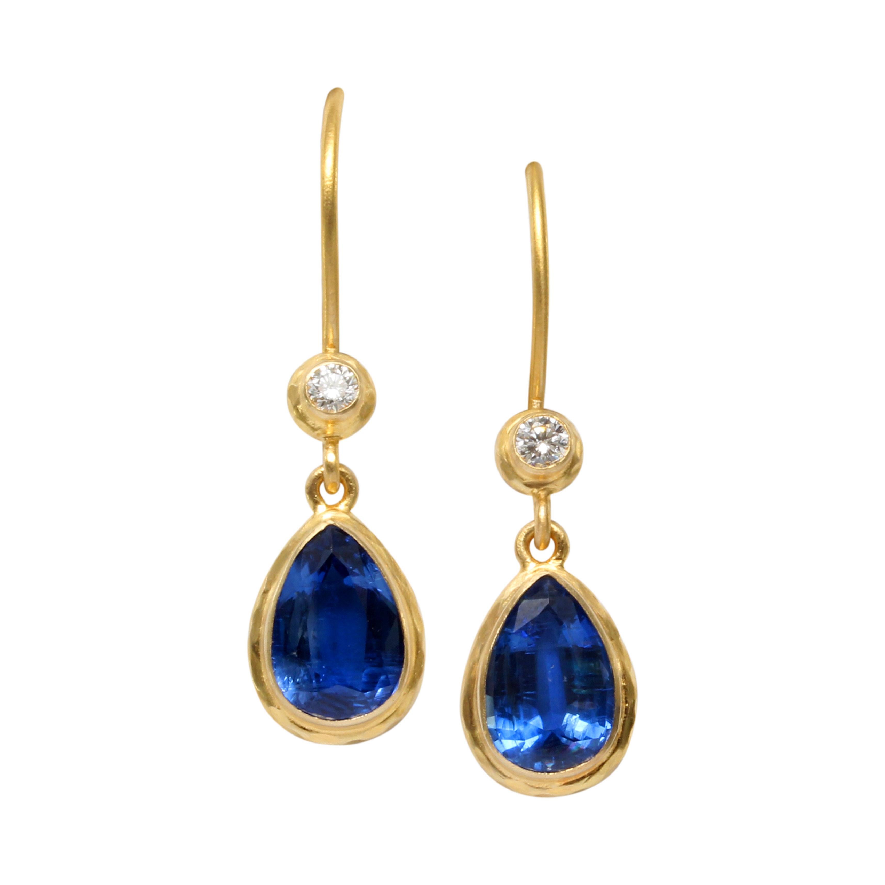 Two brilliant blue 6 x 9 mm pear shaped faceted Kyanites are surrounded by thick, slightly textured 18K gold bezels and suspended below safety-clasp 18K wires which terminate in sparkling 2.2 mm faceted VS1 diamonds in similar thick bezels which