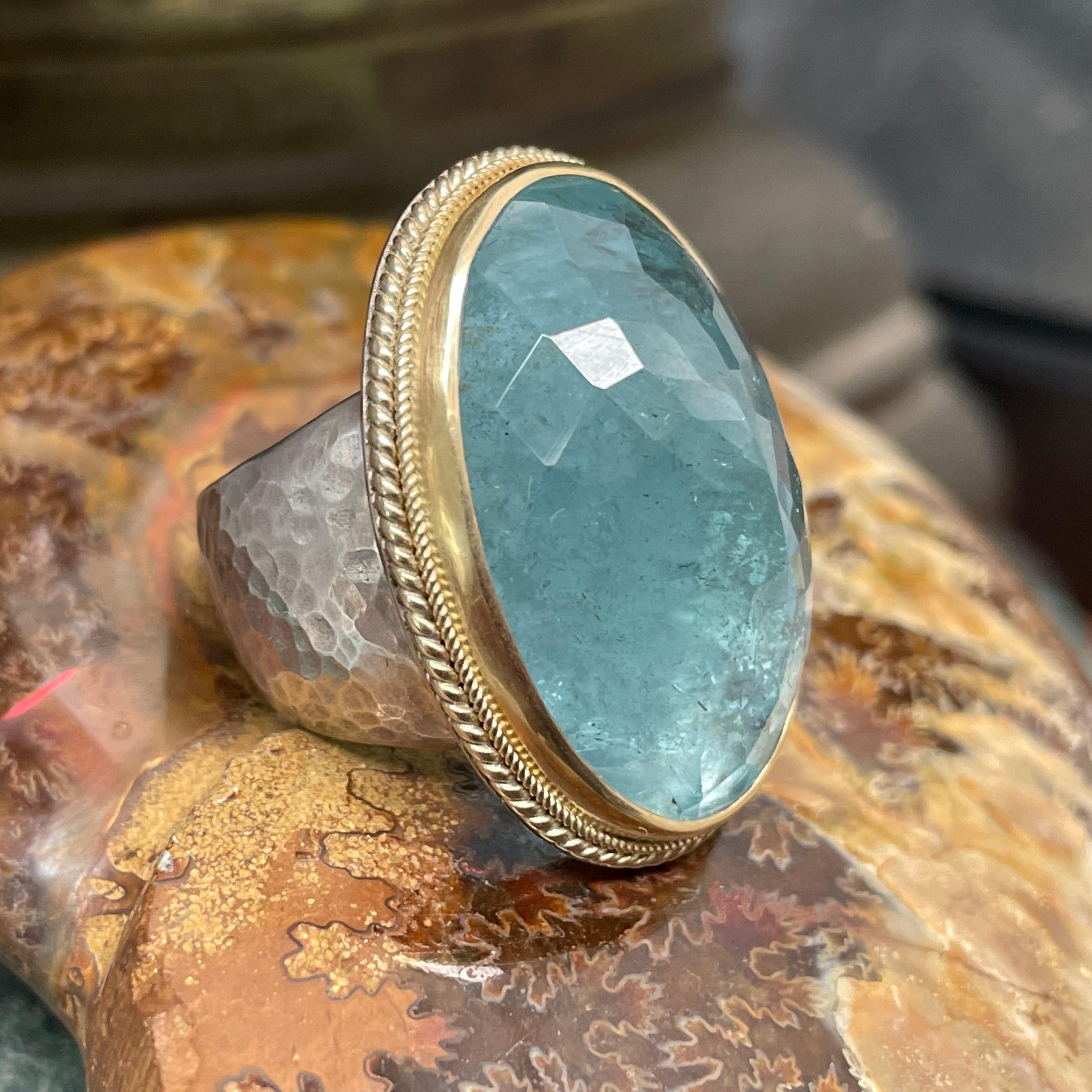 A nice light blue 20 x 28 mm oval rose cut aquamarine is held in a signature large/small double twist wire 18K setting atop a wide tapered sterling silver shank which is hammered and matte-finished. This stone glows with internal chatoyancy... The