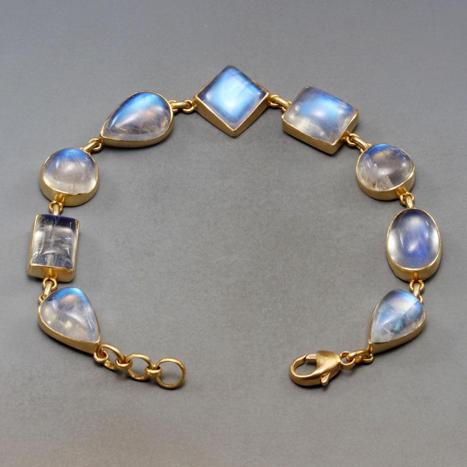 A beautiful grouping of mixed shaped irregular rainbow moonstone cabochons approximately 10 mm round to 8 x 13 mm in size are set in sightly cupped varied 18K gold bezels in this Steven Battelle designed bracelet.  These stones are super flashy with