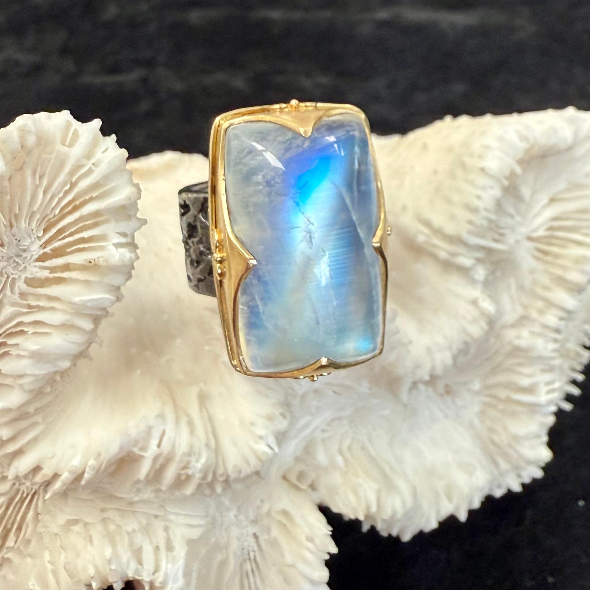An elegant 15 x 26 mm cushion shaped rainbow moonstone cabochon is held in an ancient inspired 