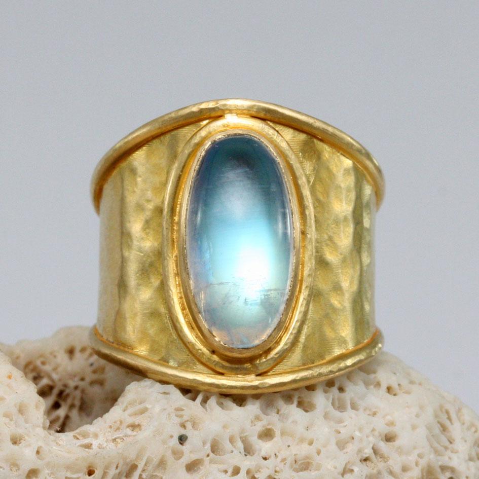 A shimmering long oval 7 x 14 mm Rainbow moonstone is set atop a simple matte-finish hammered wide band with wire delineated edges in this classic look.  This band is sized 7.  It's not easy to resize... Elegant, eye-catching, a stunner !