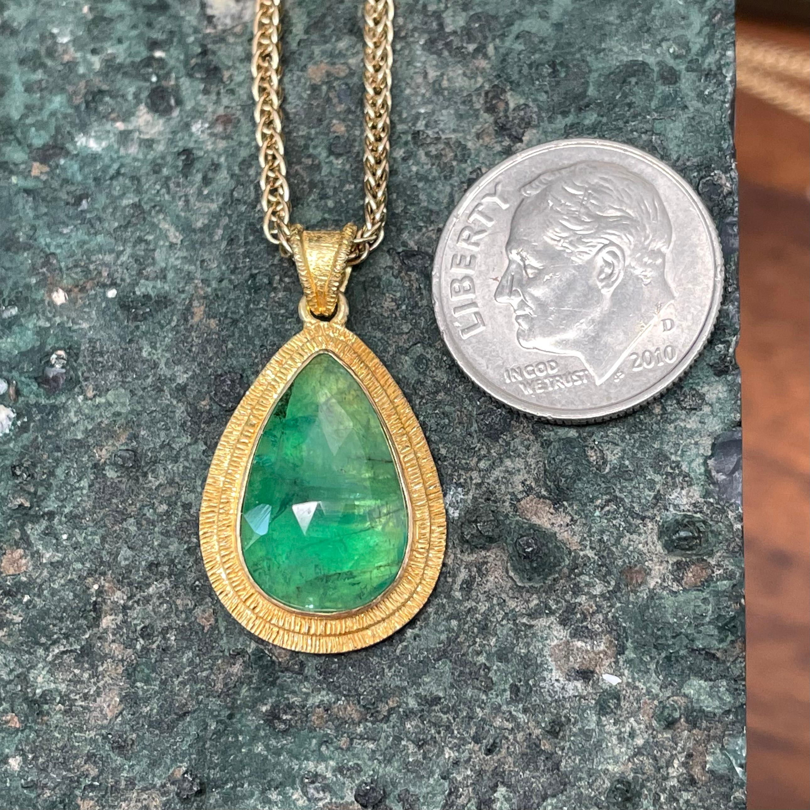 A sweet 10 x 16 mm pear shaped rose cut Zambian emerald is highlighted in an organic doubled line textured bezel with similar bail in this enchanting pendant.  A really nice splash of beautiful green. The 20 inch triple woven 18K chain shown is not