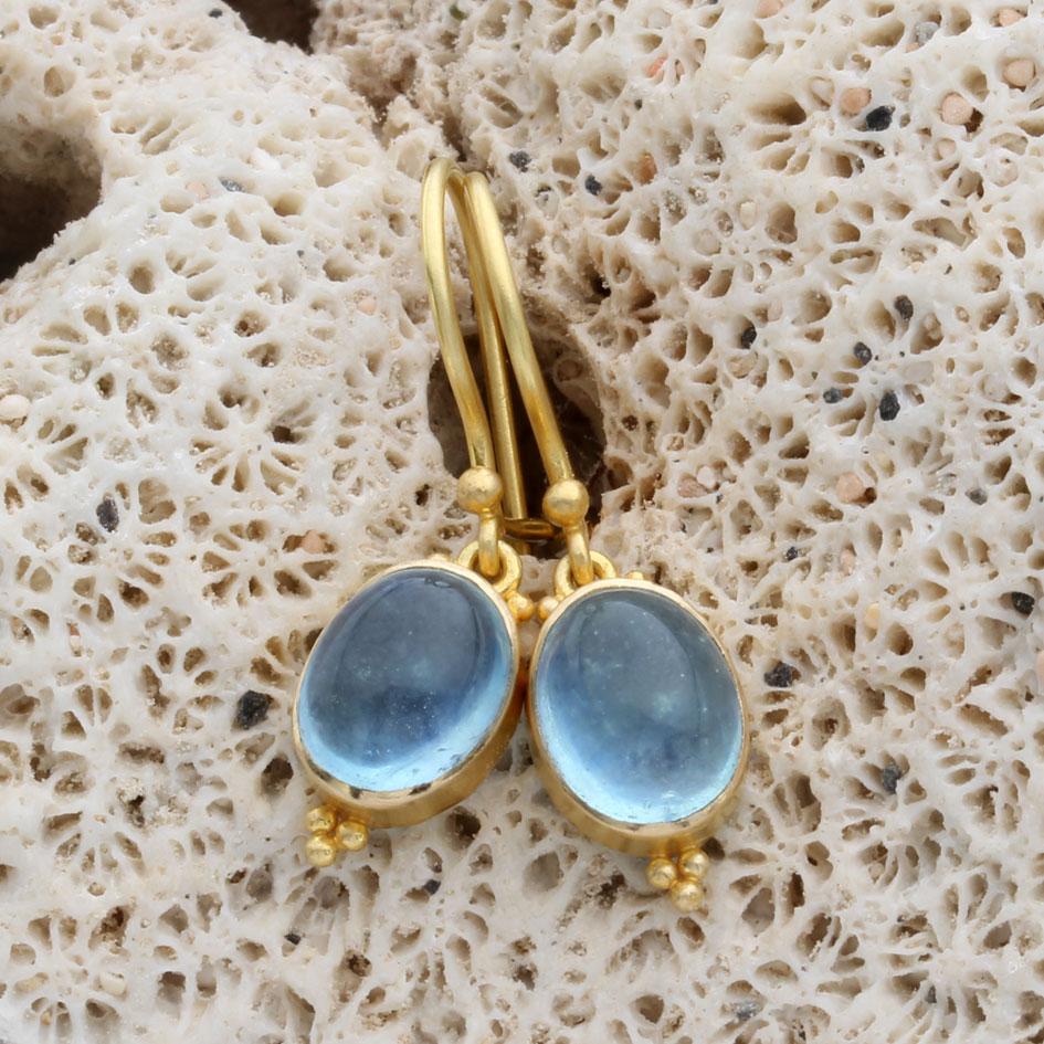 Zwei meerblaue 7 x 9 mm große ovale Cabochon-Aquamarine sind in matte 18-karätige Goldfassungen gefasst, die unter 18-karätige Goldohrringe mit Sicherheitsverschluss gehängt sind.  Die schlichten Lünetten sind mit dem klassischen