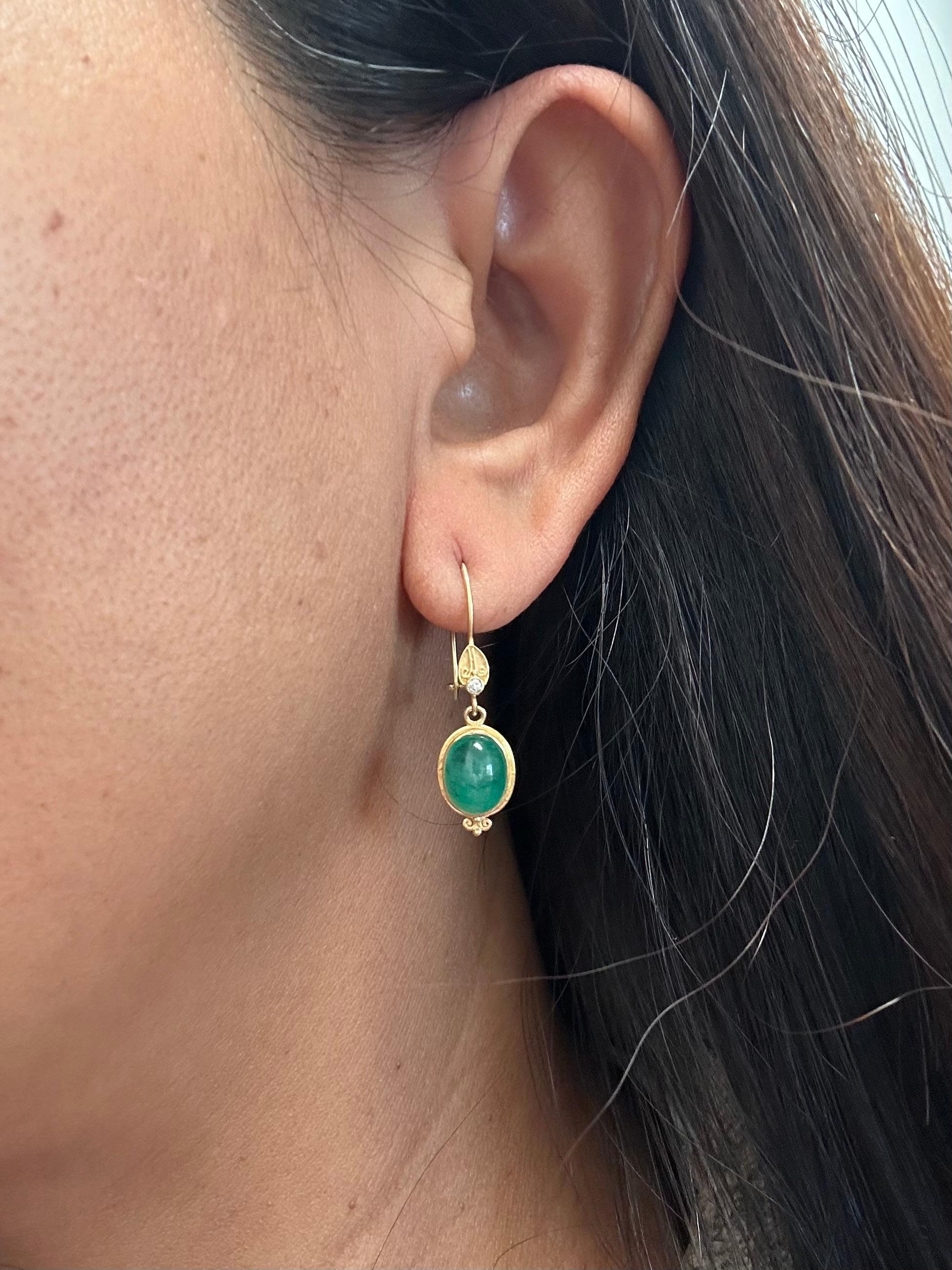 Two deep green 7 x 9 mm oval Zambian emerald cabochons are held in handmade 18K bezels surrounded by enhancing wires that end in a double scroll motif at the bottom.  At the top of the safety clasp wires, a small component with delicate