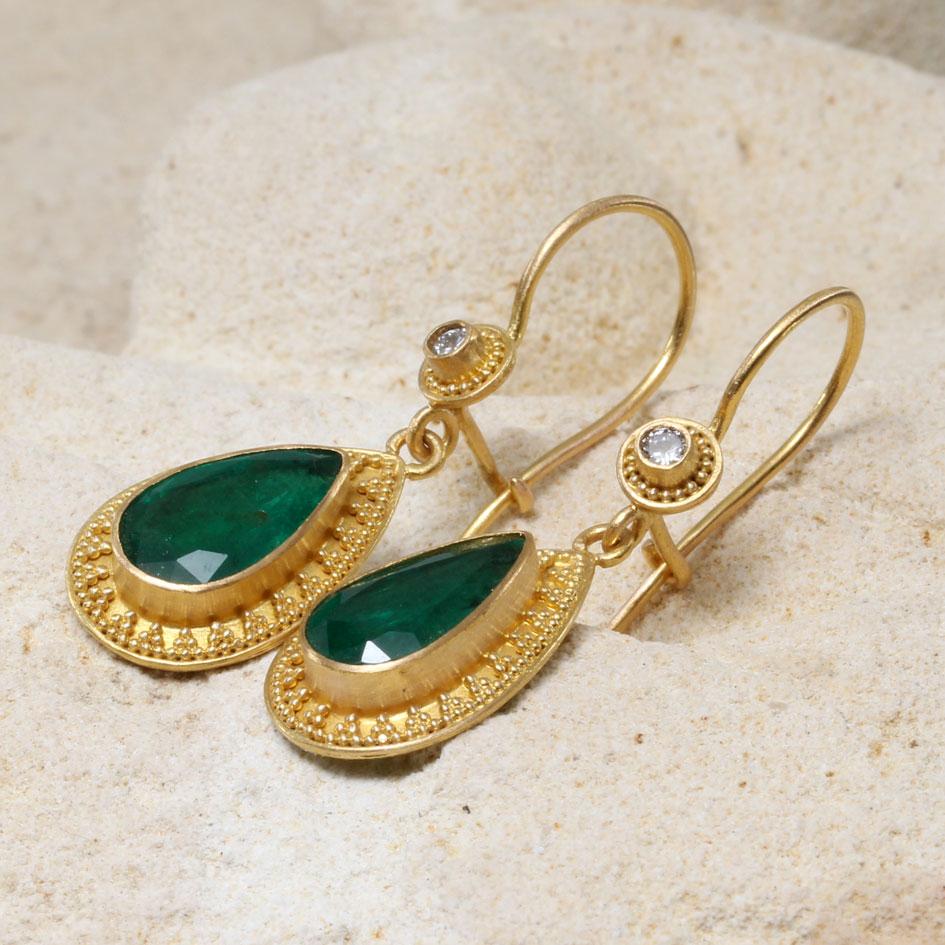 Two well matched deep green Zambian 7 x 12 mm long pear-shaped faceted emeralds are highlighted by encompassing geometric high-karat 22K gold granulation and dangle below sparkling 2.2 mm VS1 diamonds with concentric granulation surrounding at the