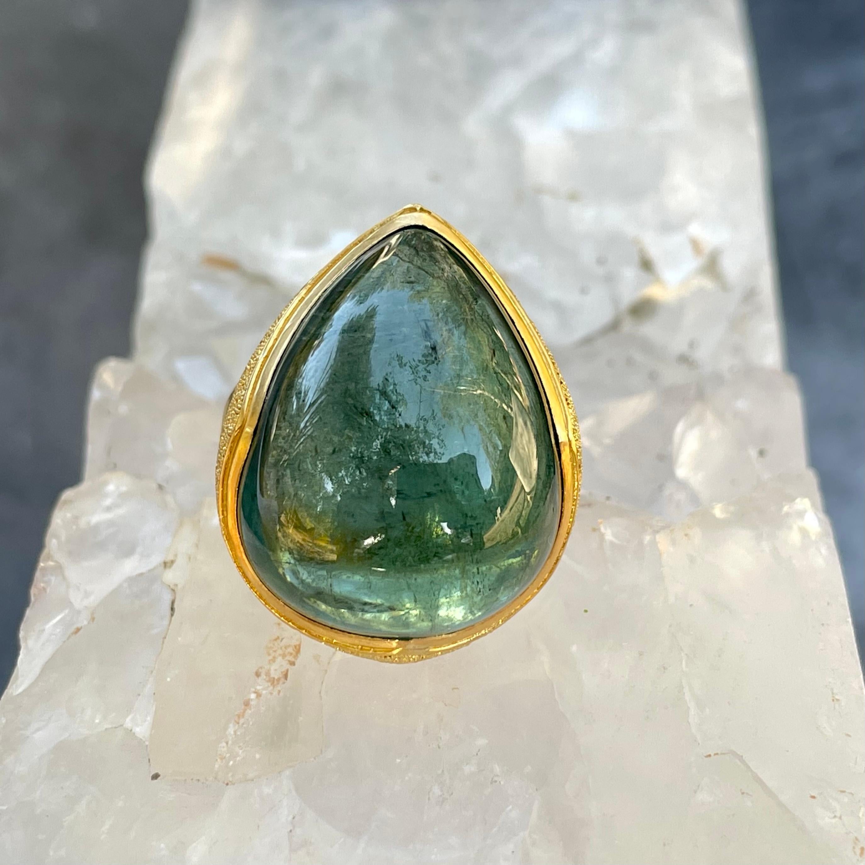 A large, juicy, gumdrop of a Brazilian blue-green indicolite tourmaline (one of the rarest colors of tourmaline) is held lovingly in a signature Steven Battelle ancient-inspired 