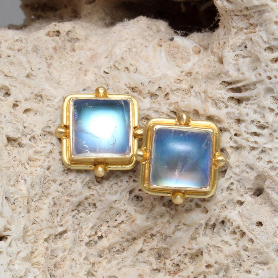 Two blue shimmering 7 mm square rainbow moonstones are set in 18K gold bezels and surrounded by round gold wire with spaced 