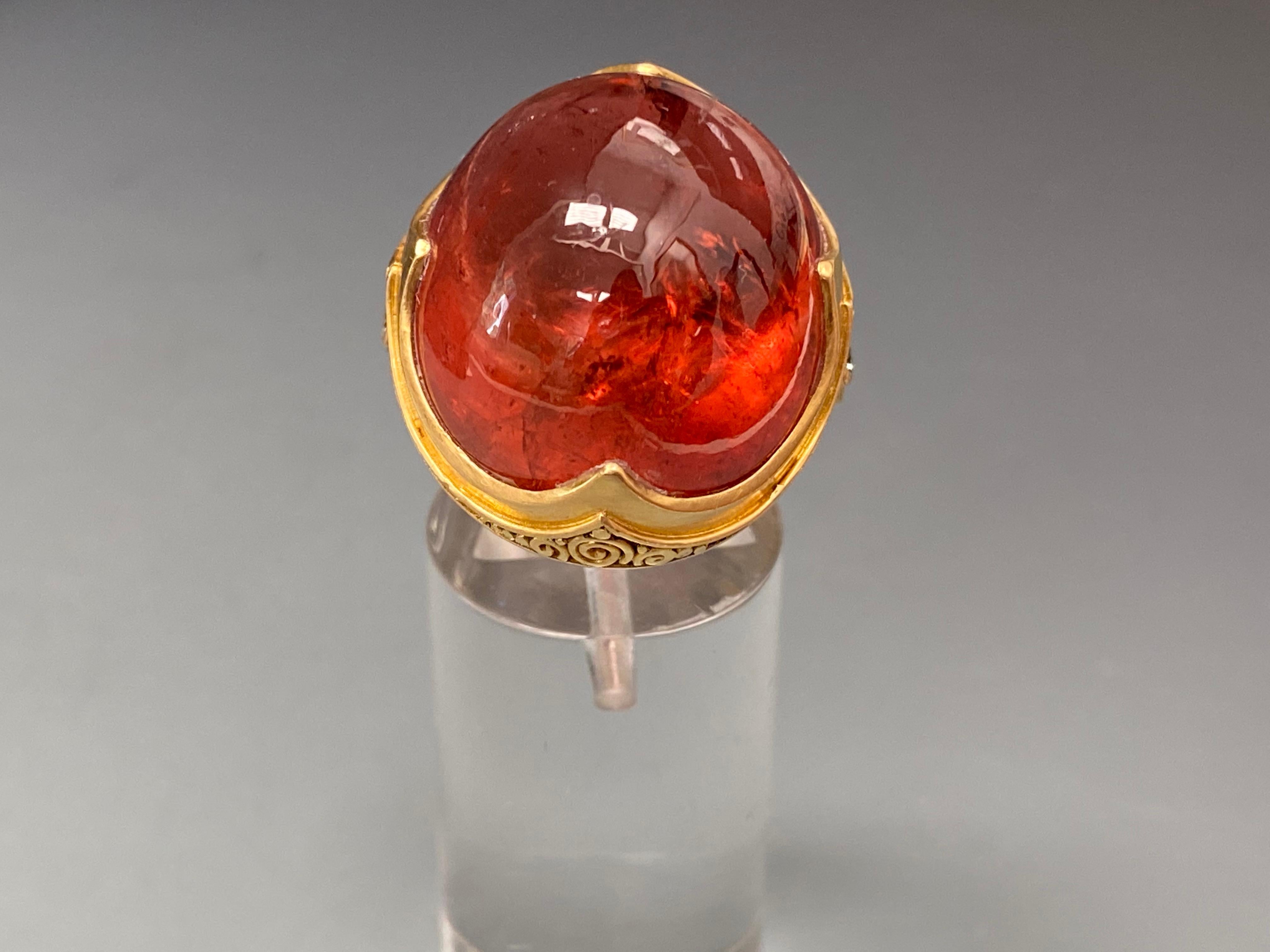 A deep rich orange-pink gumdrop of Brazilian tourmaline, 20x22 mm in size is the centerpiece of this beautiful showstopper ring by Steven Battelle.  Accented with two 2mm flanking diamonds and inset scroll wire work in a signature 