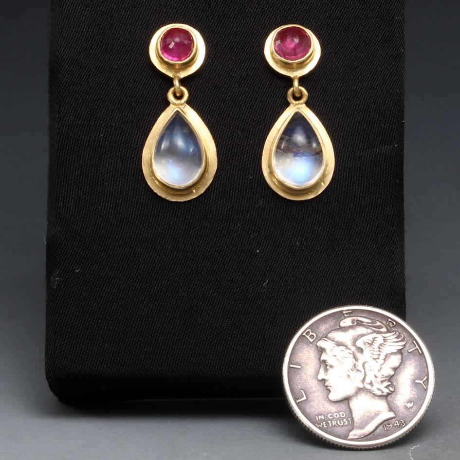 Two blue shimmering 6 x 9 mm pear shaped rainbow moonstone cabochons dangle below deep pink 4 mm rose cut rubies in this elegantly simple 18K gold post earring design.  All the stones are surrounded by wide matte-finish gold double bezels for a