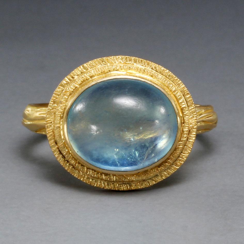 A deep blue 10 x 12 mm oval cabochon aquamarine is set horizontally within stepped 