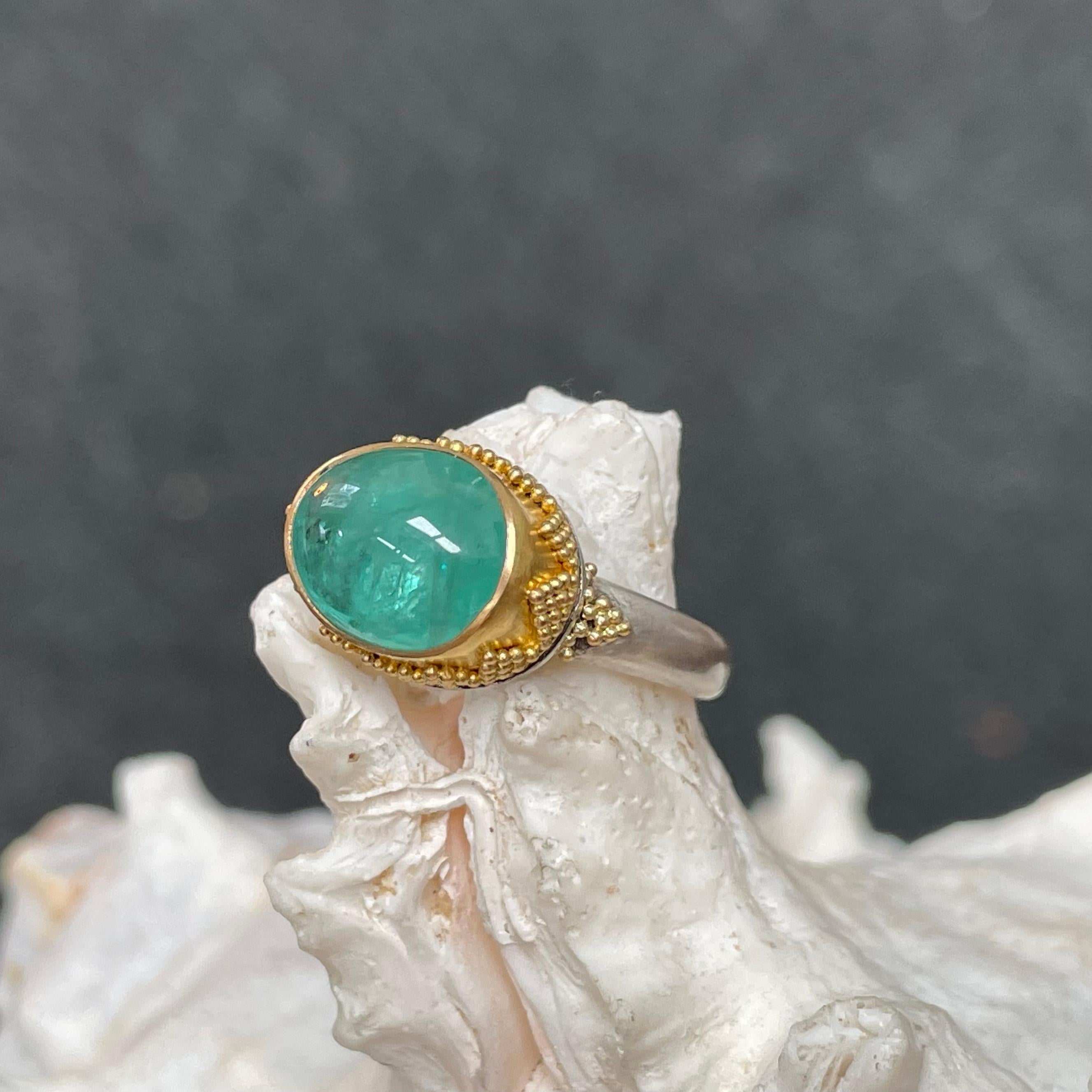 A beautiful 9 x 12 mm light green oval cabochon emerald is showcased within a cupped 22K bezel and geometrically granulated 