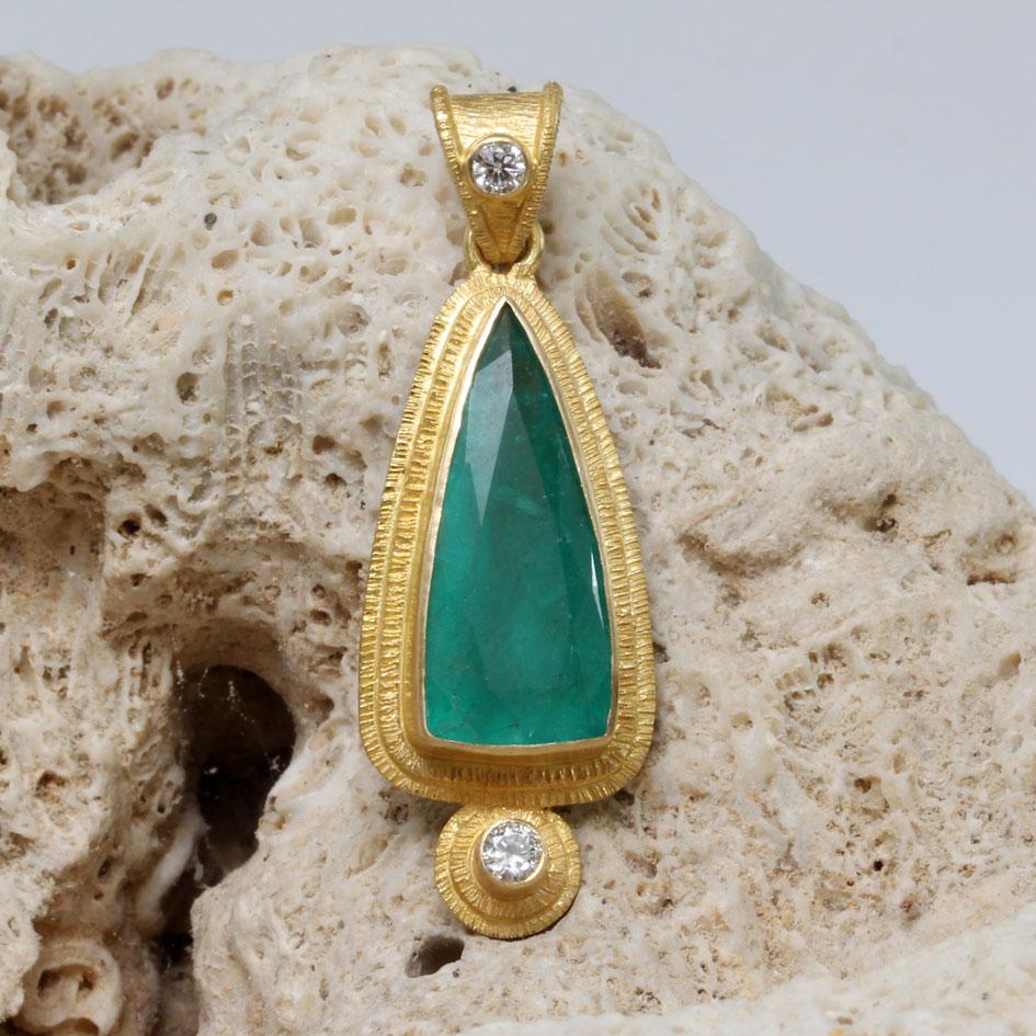 Une grande émeraude triangulaire à facettes de 8 x 19 mm est mise en valeur par une double rangée de lignes texturées fabriquées artisanalement.  Lunette en or 18K qui l'entoure, avec un diamant de 2,5 mm VS1 scintillant.  avec une texture similaire