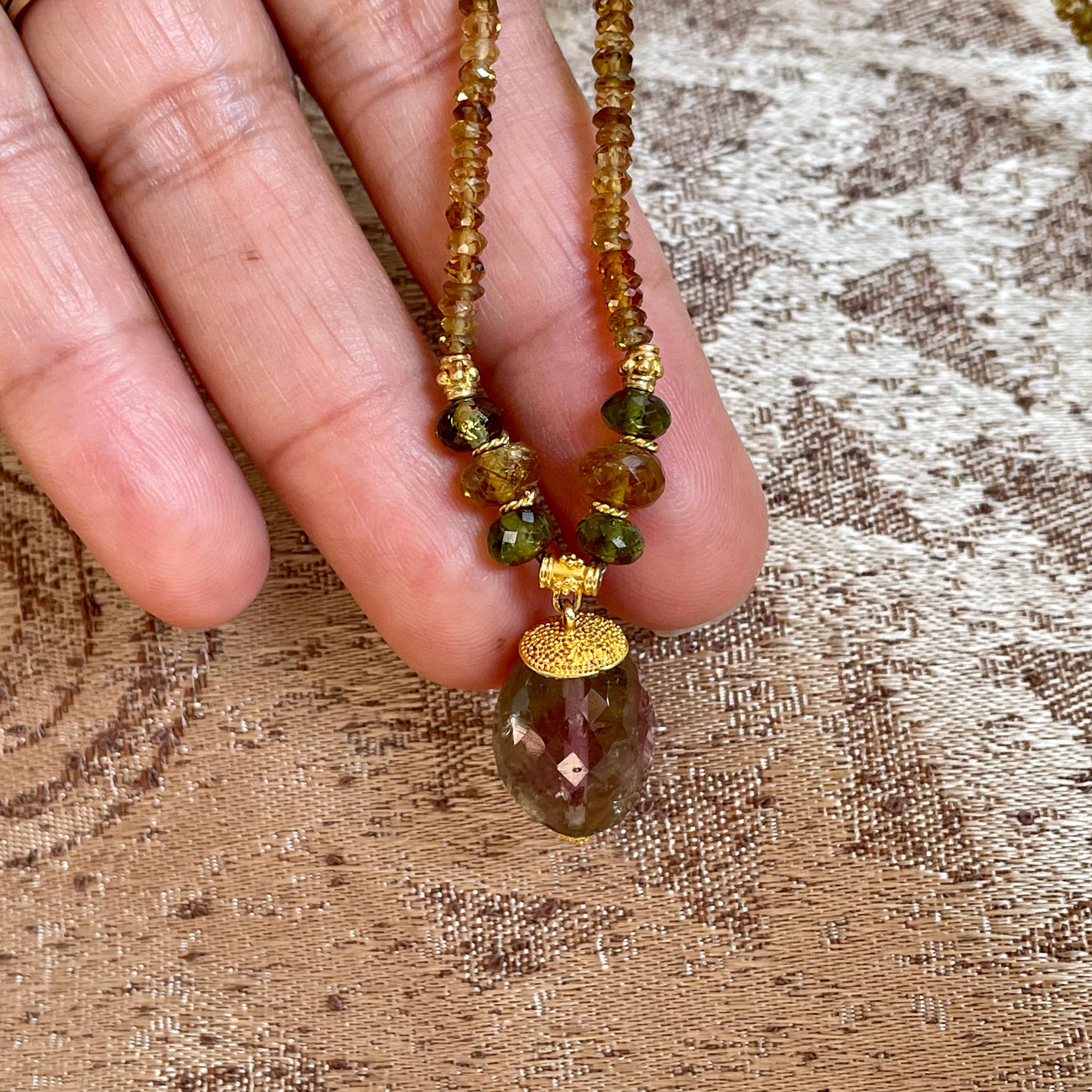 A 12 x 19 mm watermelon tourmaline briolette faceted bead with flashes of green and pink is held by 22K granulated caps and suspended below a string of greenish and orangish tundra sapphire beads with larger tourmaline beads and 22K spacer beads