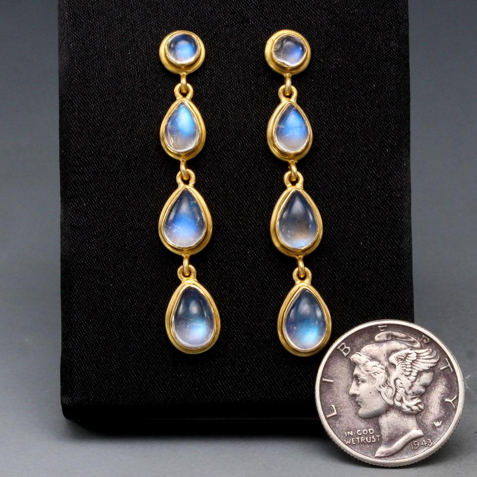 Graduated sized (4 x6 mm to 6 x 8 mm) pear shaped cabochons of shimmering rainbow moonstone are set in rich rounded double bezel settings and dangle below 5 mm rainbow moonstone posts in this design.  The gold and blue of the moonstones a wonderful