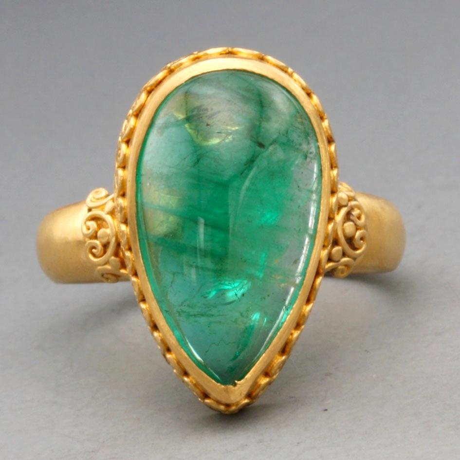 A lively, bright green 10 x 19 mm pear shaped emerald cabochon is cradled  in a fine handmade high karat gold bezel decorated with a delicate 