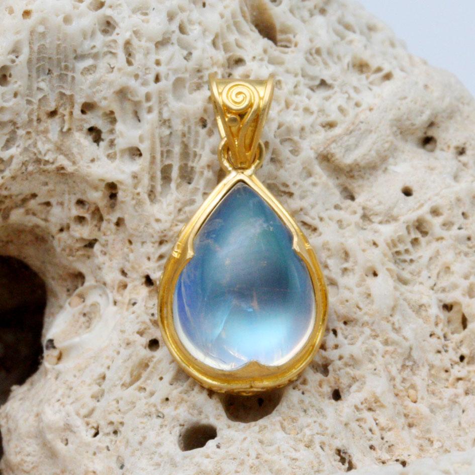 Un cabochon de pierre de lune arc-en-ciel en forme de poire de 9 x 12 mm, d'un bleu lumineux, est serti dans une monture.  