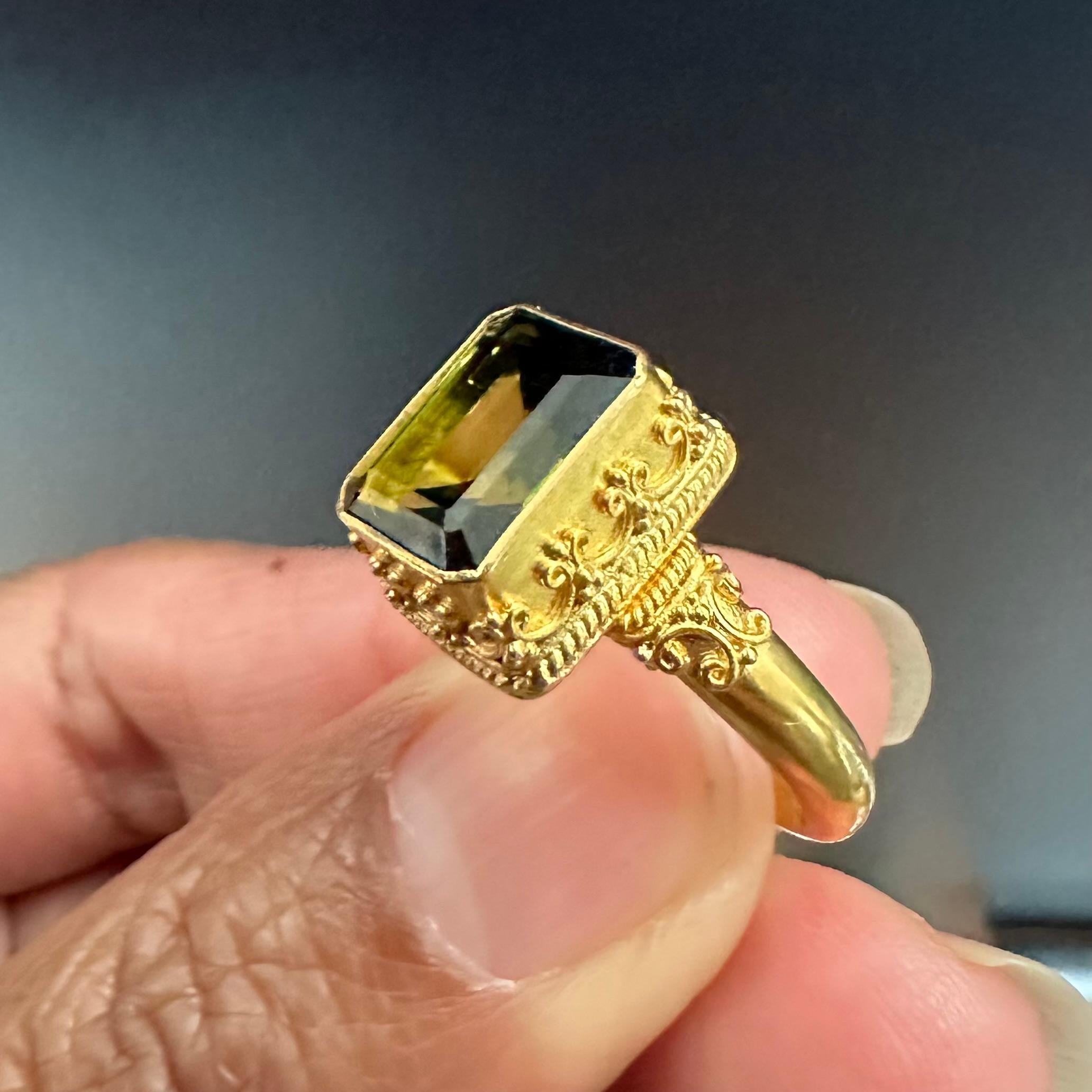 Une tourmaline vert olive de 10 x 12 mm à facettes octogonales est sertie dans un chaton merveilleusement orné sur une tige légèrement effilée de finition mate avec un motif assorti similaire.  Cette bague met vraiment en valeur les compétences