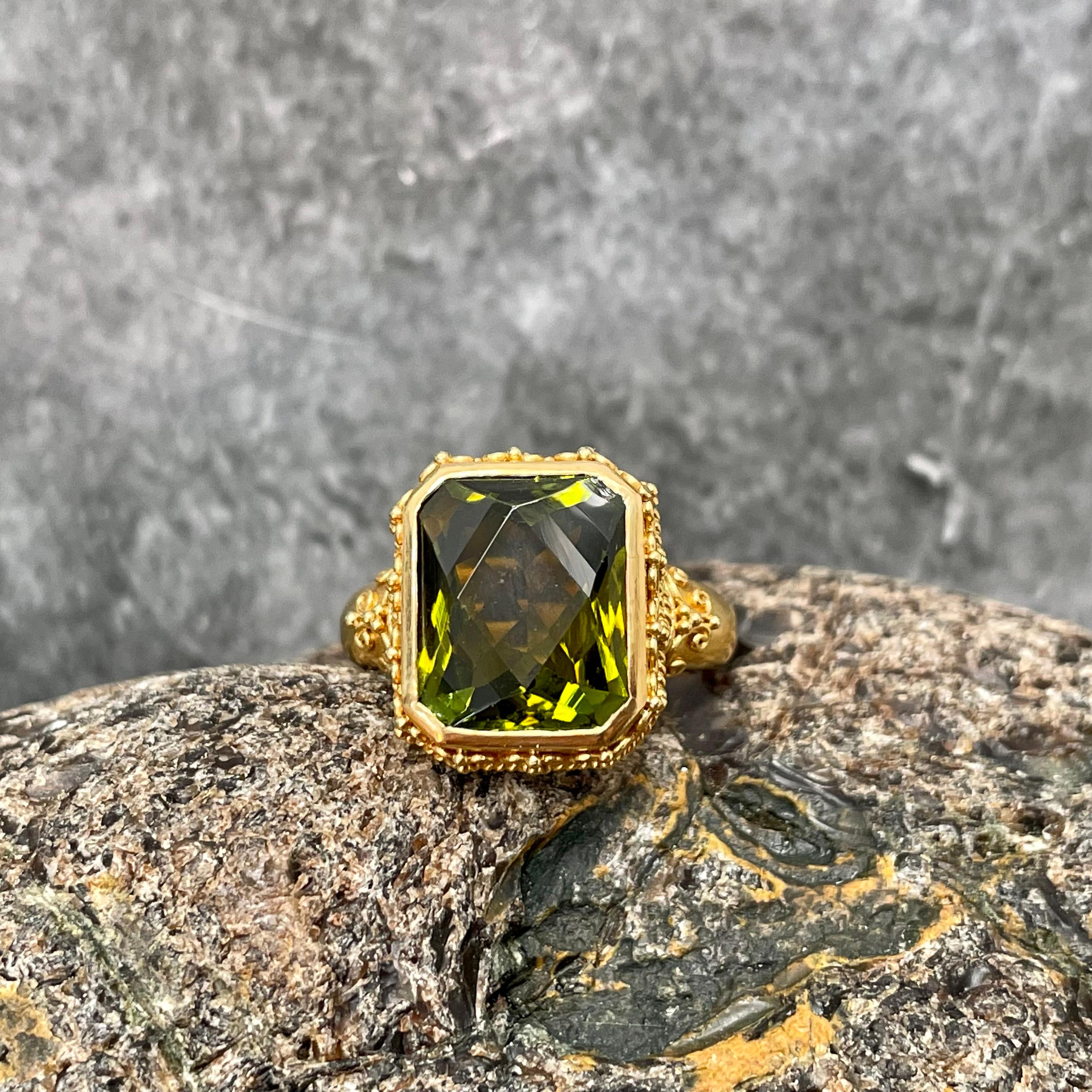 A fancy cut 10 x 12 mm olive colored octagonal green tourmaline is held with intricate ancient-inspired fine hand applied wire work and granulation in this masterpiece of artisanal high-karat gold smithing.  The slightly tapered matte-finish band