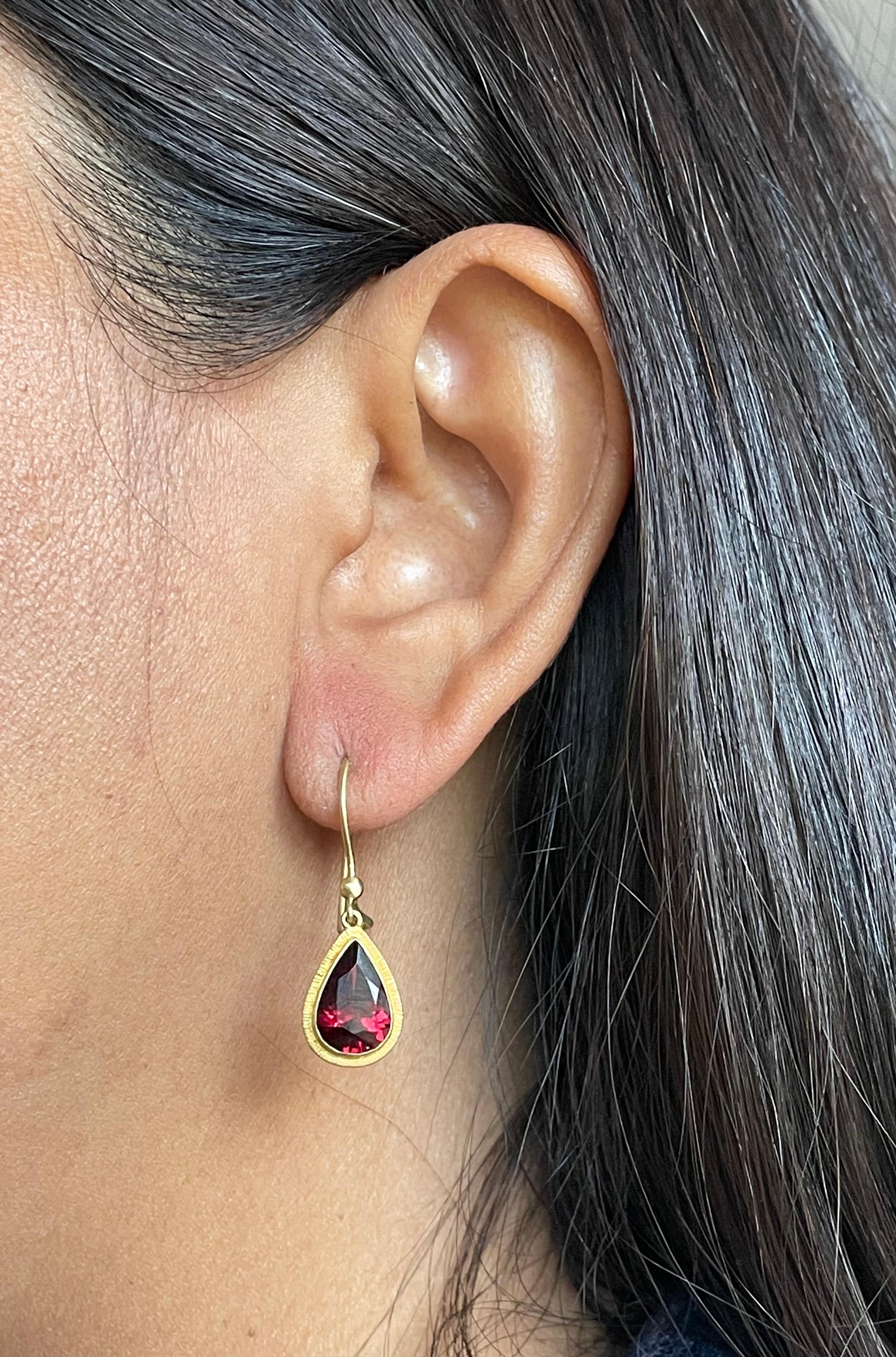 Two flashing 7 x 12 mm faceted pear shaped garnets are surrounded by line textured 18K gold bezels and suspended below small half round balls on safety clasp wires, in this simple and elegant design sure to please.  The brilliant red of the garnets
