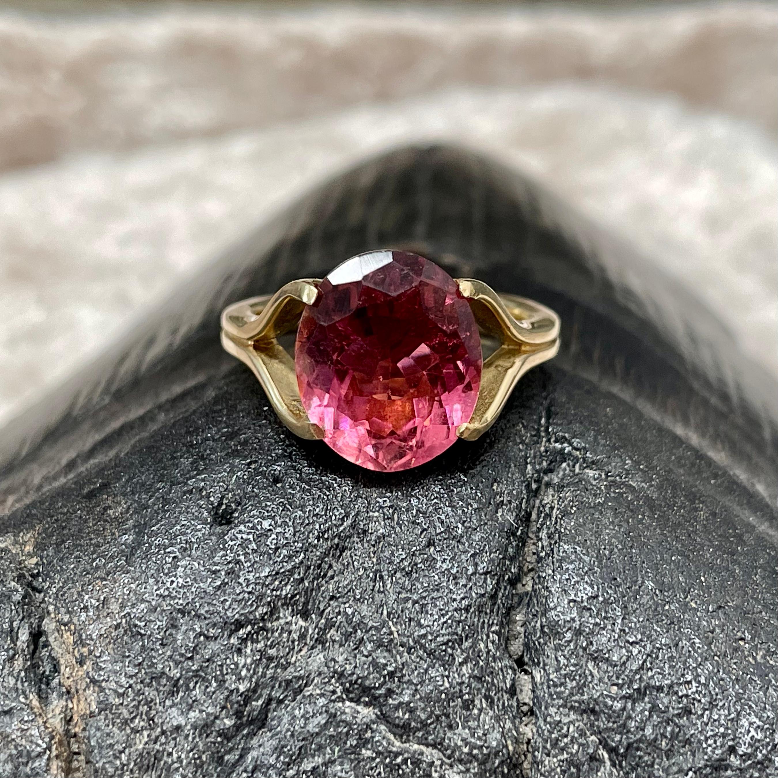 A bright 10 x 12 mm faceted oval Brazilian pink tourmaline floats almost magically above an interesting curved and split shank designed 18K ring. 
A really modern and  clean presentation of this beautiful bright pink stone.  This ring is currently