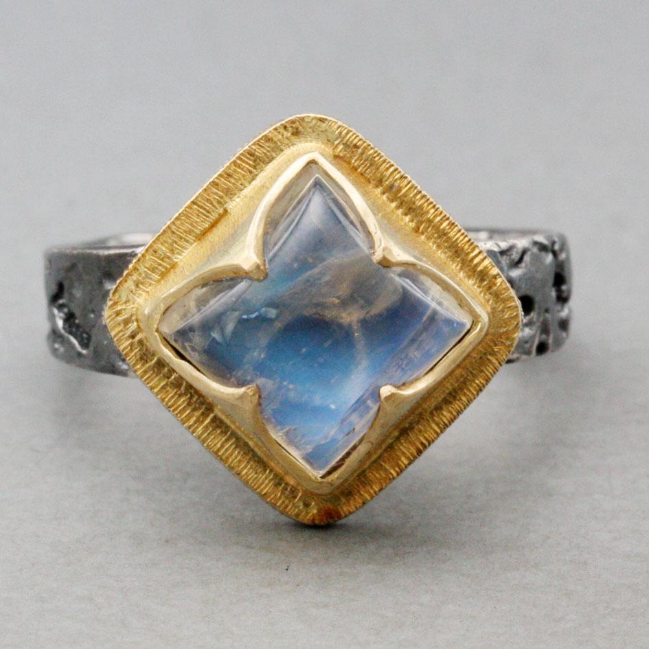 A high domed 9 mm square rainbow moonstone is set at a 45 degree angle in a 