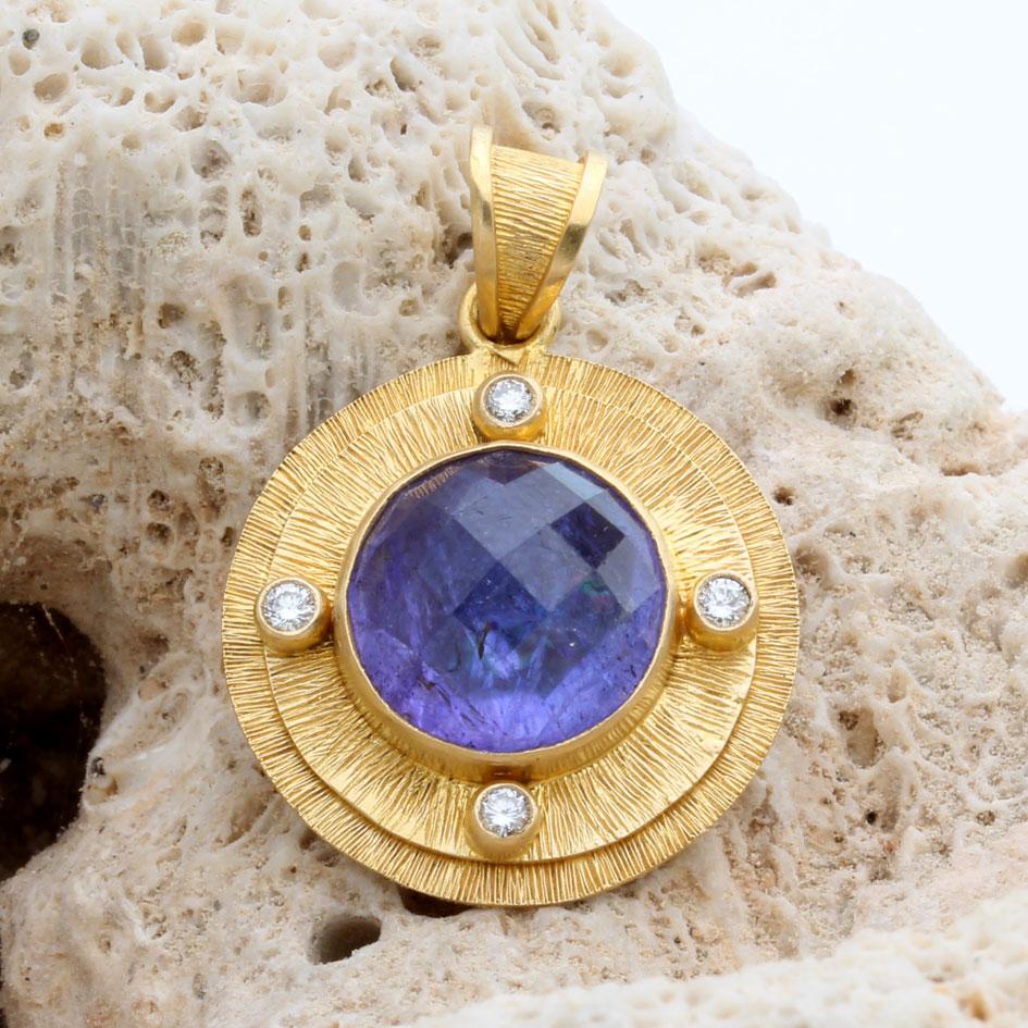 Una tanzanite rotonda rosa sfaccettata blu-viola di 11 mm è incastonata in un castone in oro 18 carati e circondata da due castoni concentrici a gradini e linee con diamanti scintillanti VS1 di 1,9 mm montati nelle direzioni cardinali.  La cauzione
