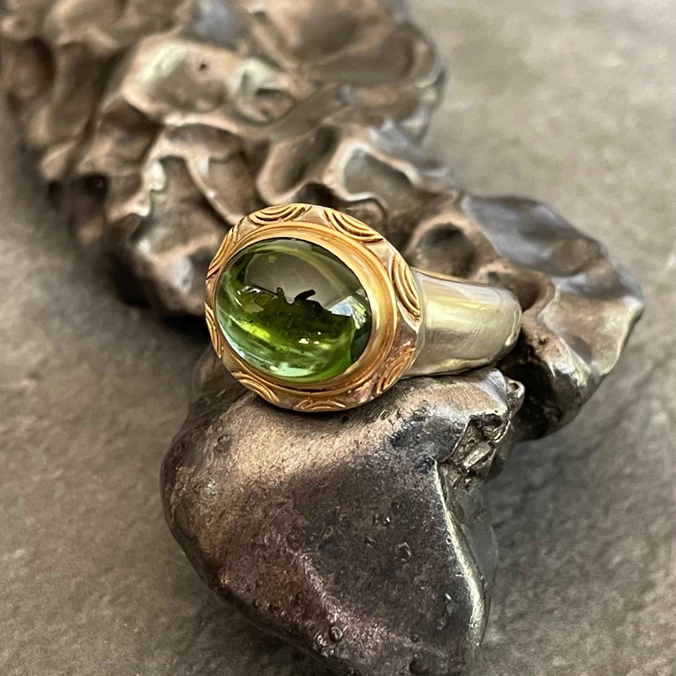 A beautiful 10 x 12 mm clear Brazilian green tourmaline cabochon  is held in an 18K yellow gold bezel with double wire accents surrounding atop a matte-finish 14K white gold tapered shank in this intriguing design.  This ring is currently sized 6.5