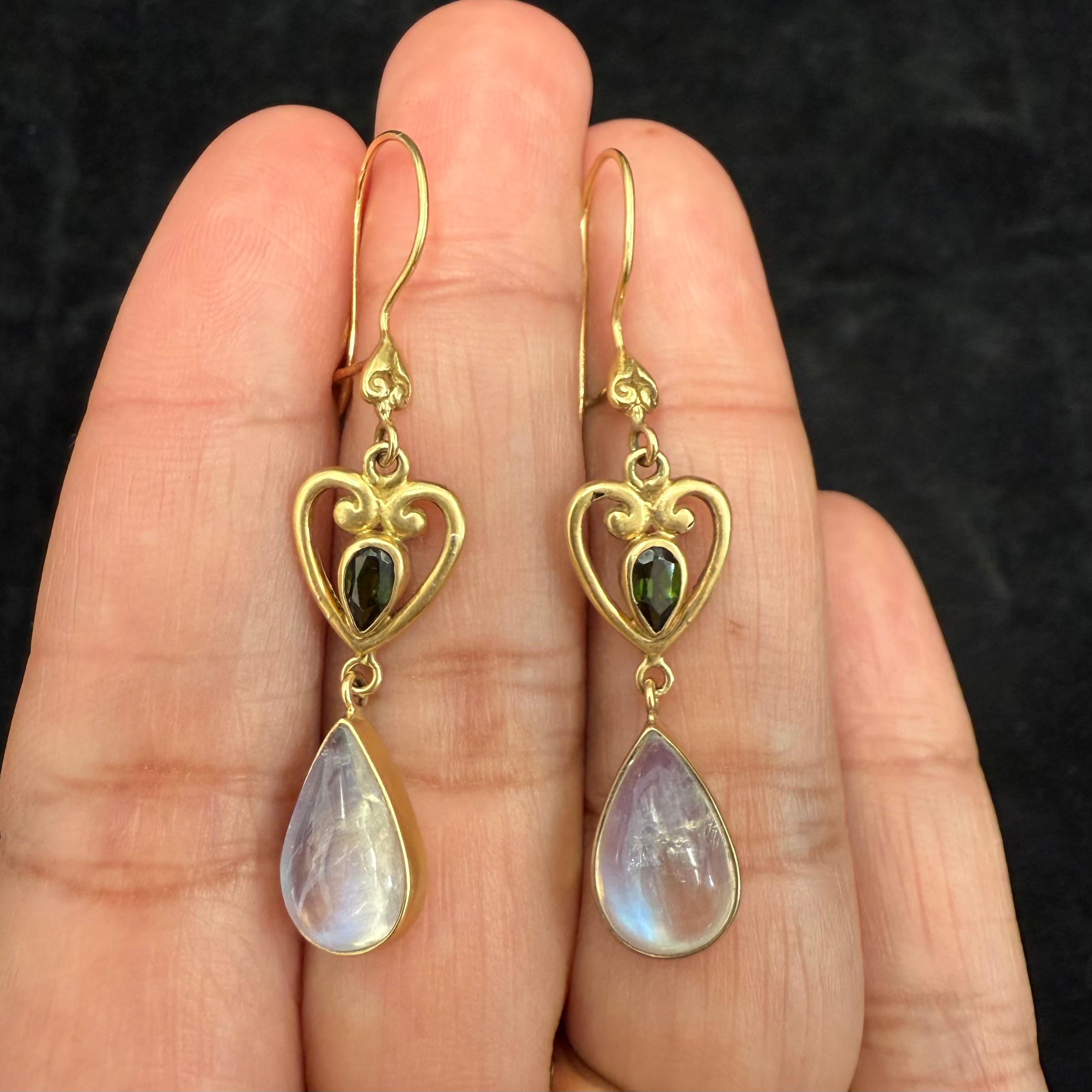Two shimmering 8 x 12 mm rainbow moonstone pear shaped drops totaling 5 carats are suspended below heart shaped gold components with central small 3 x5 mm faceted green tourmalines in this Steven Battelle design. Safety clasp wires. 
