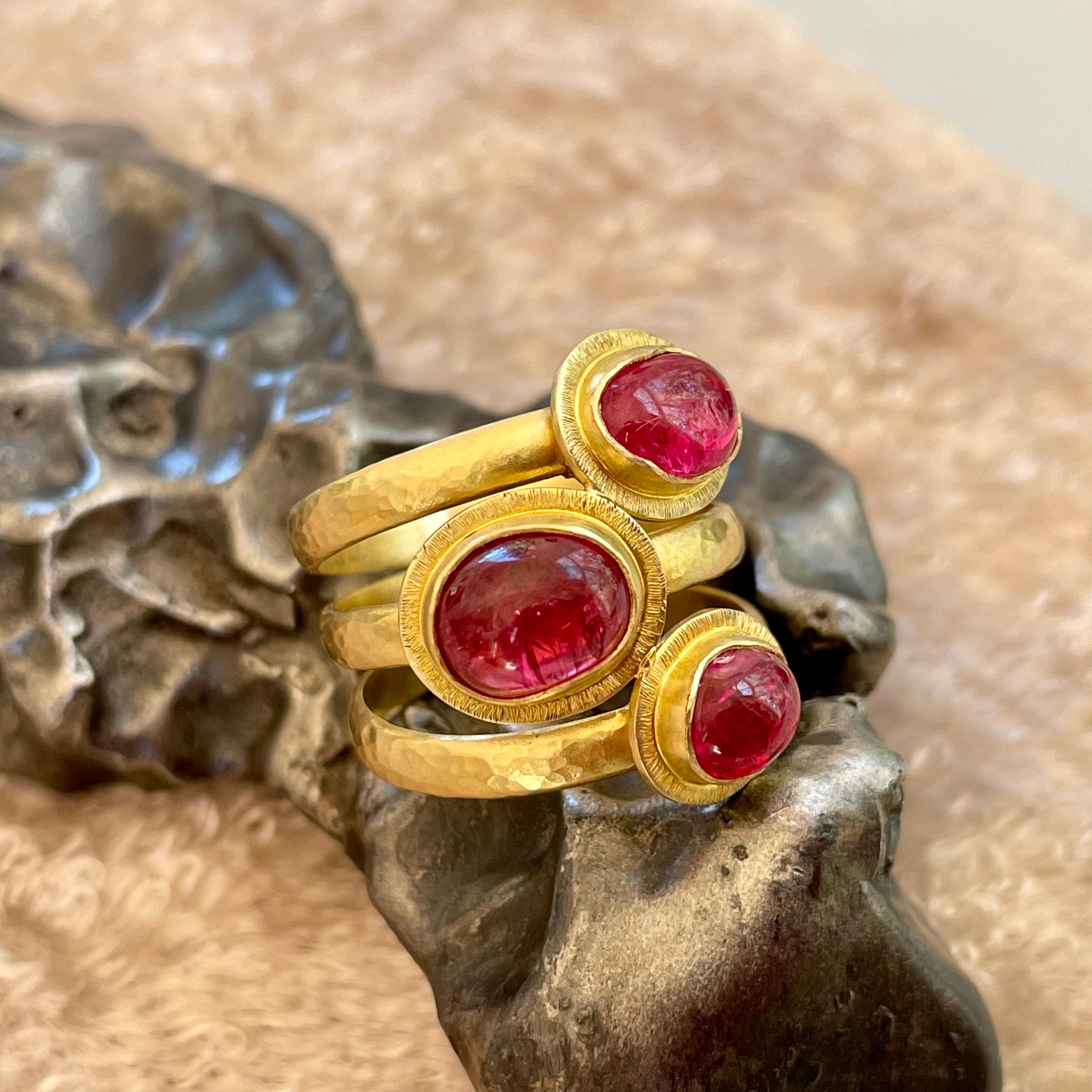 Three organically shaped approximately  6 x 8 mm bright pink Spinel cabochons are set surrounded by irregular line textured bezels on hammered and fused individual bands to create this attractive ancient-inspired piece that could have been found in