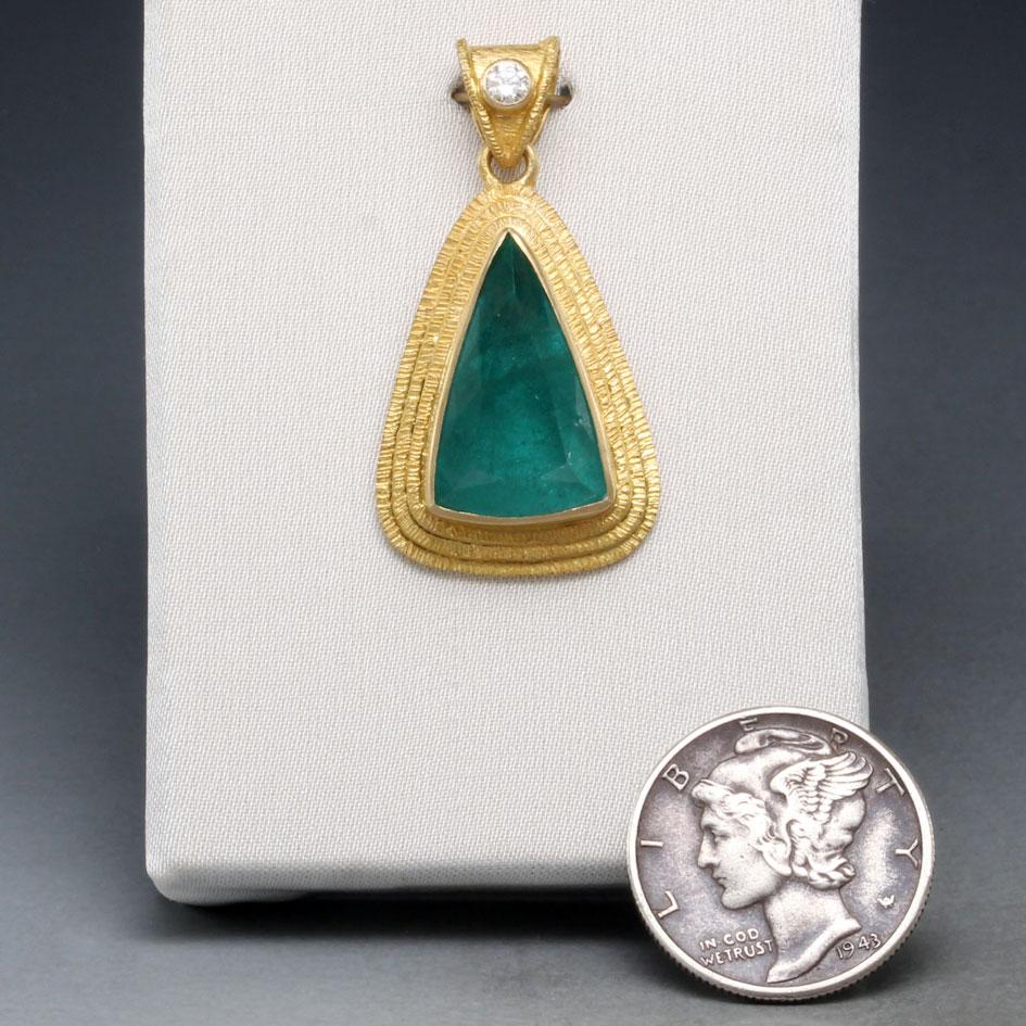 An exquisite 10 x 16 mm triangular faceted emerald from the Itabira mines in Minas Gerais, Brazil is mounted within a triple layer 