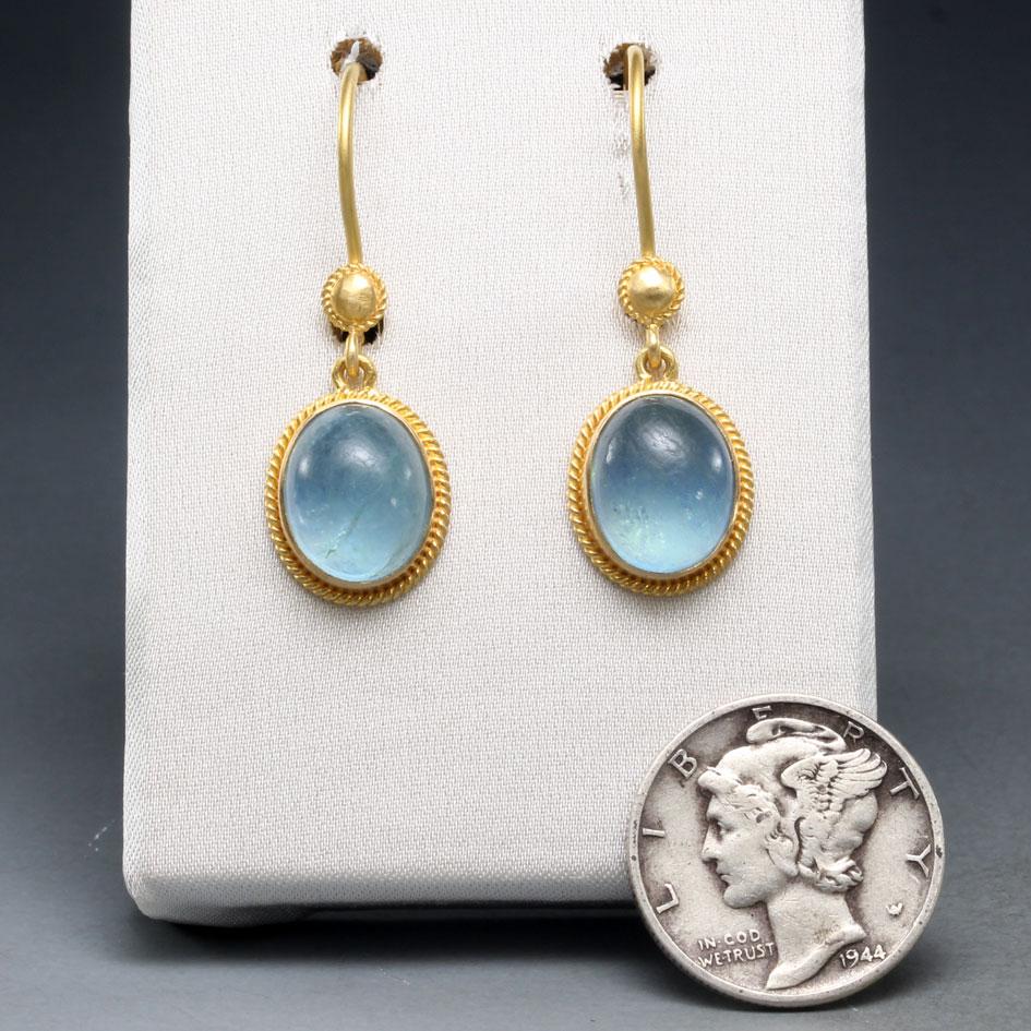Due acquemarine cabochon blu brillante di 8 x 10 mm sono incastonate in castoni d'oro 18 carati lavorati artigianalmente e circondati da ornamenti 