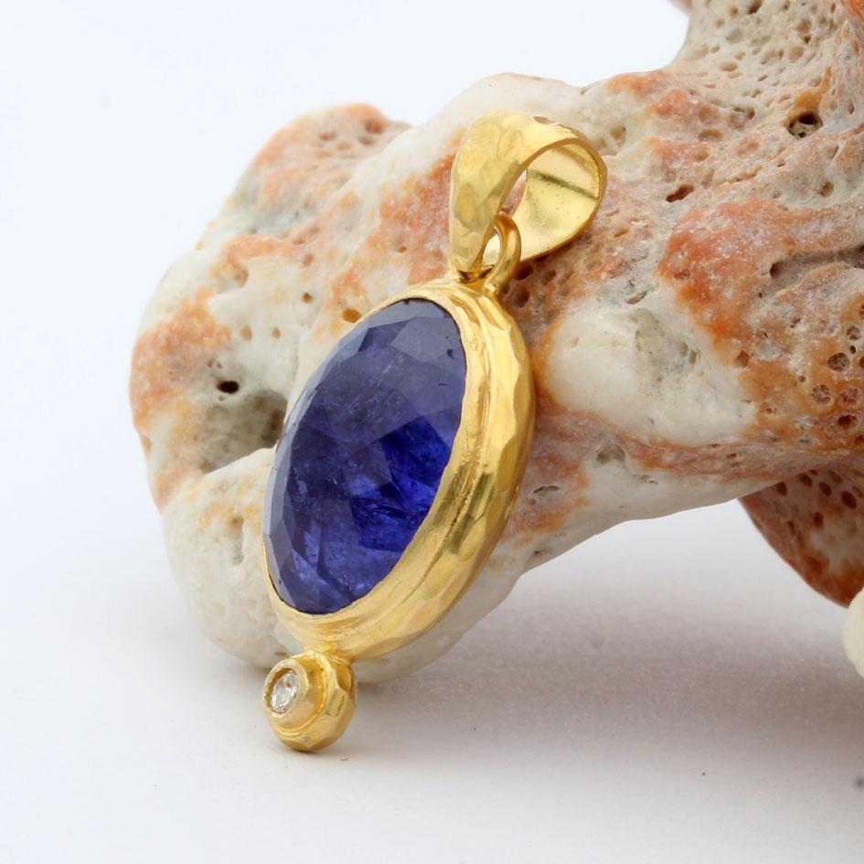 A lively 10 x 13 mm oval briolyte cut tanzanite is set in a hammered artisan crafted 18K gold double bezel setting with a 2 mm VS1 diamond accent at bottom.  The bail is also hammered to match.
A great organic setting to highlight the deep