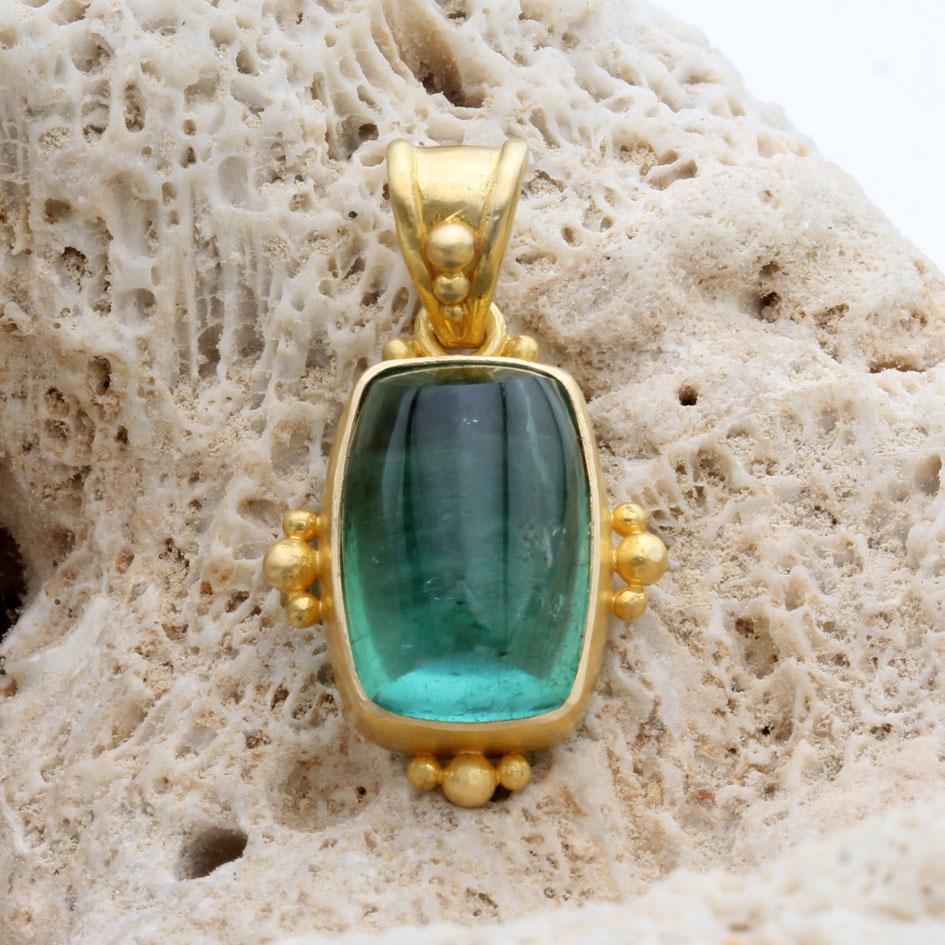 A vibrant 9 x 13 mm cushion shaped green tourmaline cabochon rests in ancient inspired artisan crafted 18k gold with handset large/small 