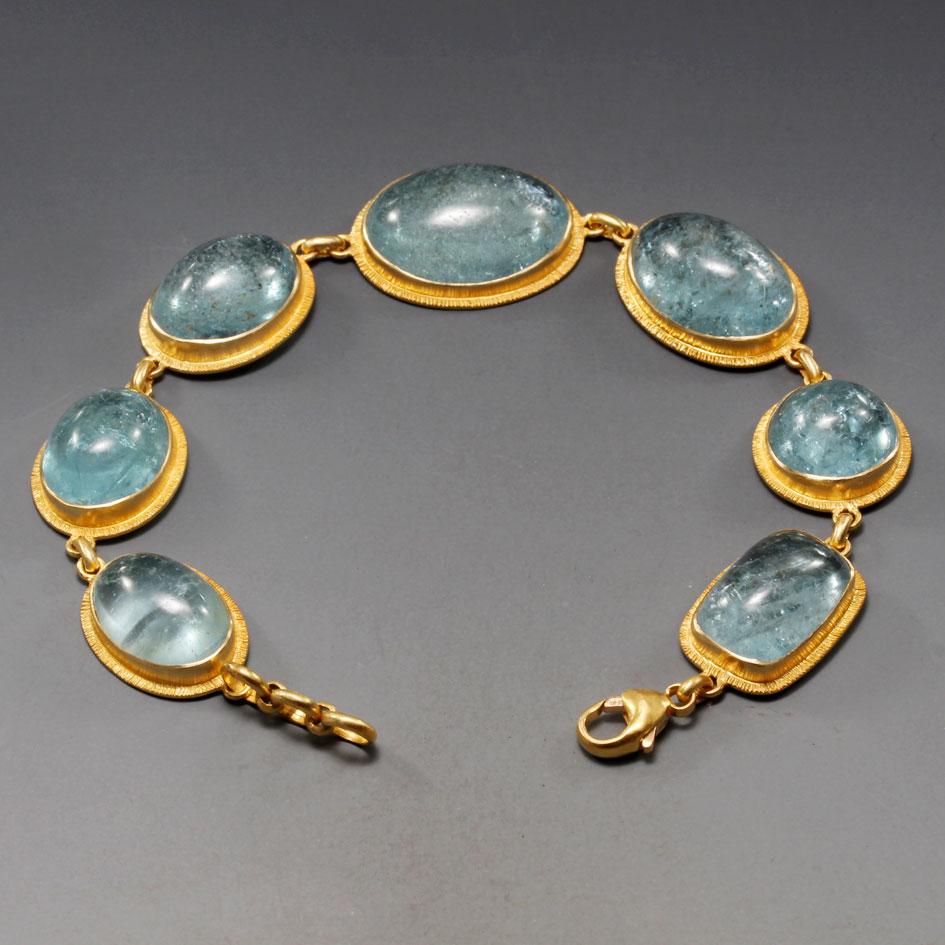 Seven large mixed shaped cabochon aquamarines from 12 x 16 mm oval to 12 mm round are displayed in artisanally crafted 
