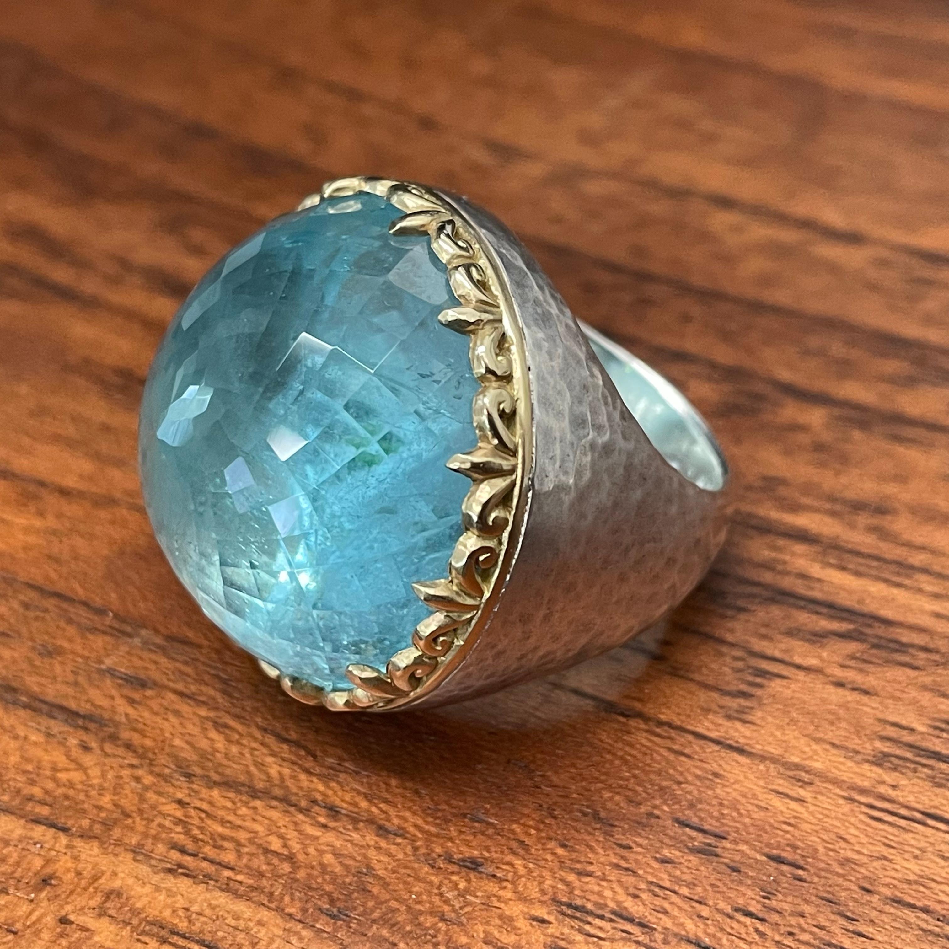 A fabulous 27 mm round rose cut Brazilian aquamarine draws attention in this Steven Battelle creation featuring a hammered matt finish shank and intricately carved multi spiraled solid 18K bezel.  Truly one of a kind.  A substantial piece of 42