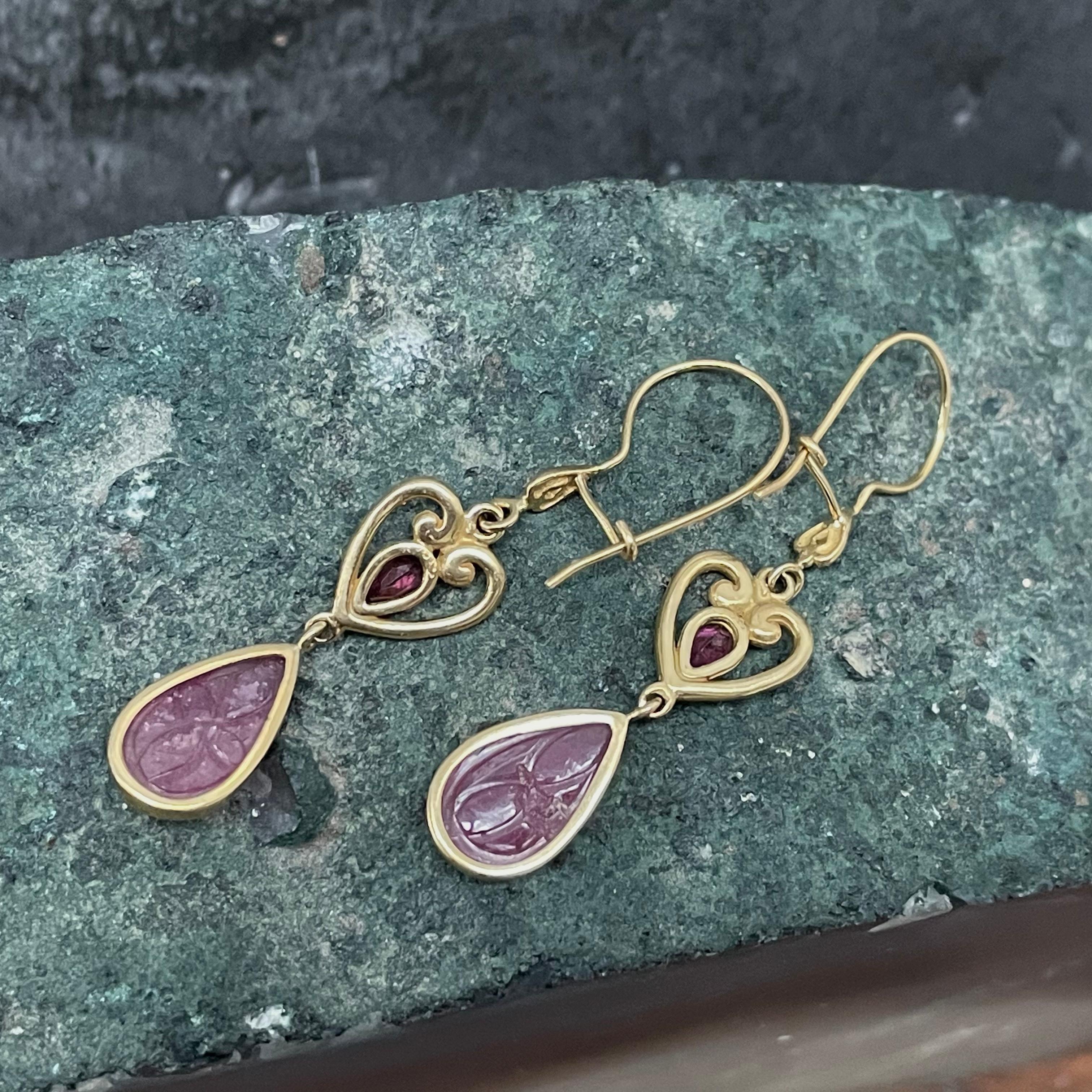 Two 8 x 12 mm pear shaped floral carved rubies dangle below heart shaped carved gold components with small faceted pink tourmaline pear accents in this one of kind earring design. 