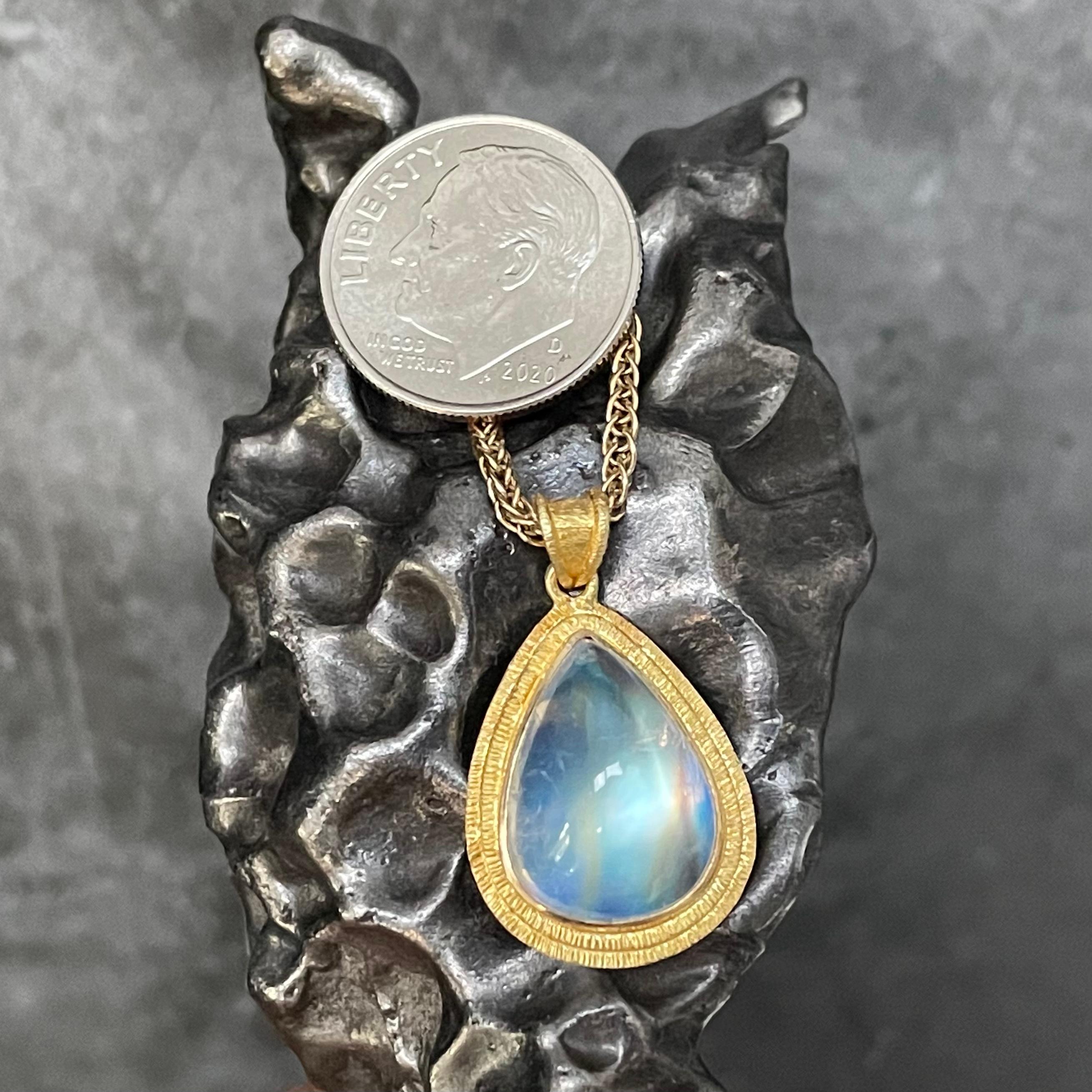 Un cabochon de pierre de lune arc-en-ciel en forme de poire de 11 x 14 mm est serti dans un cadre Steven Battelle à texture double ligne dans ce pendentif classique.  J'aime la pierre de lune arc-en-ciel pour ses propriétés magiques. Super sympa ! 