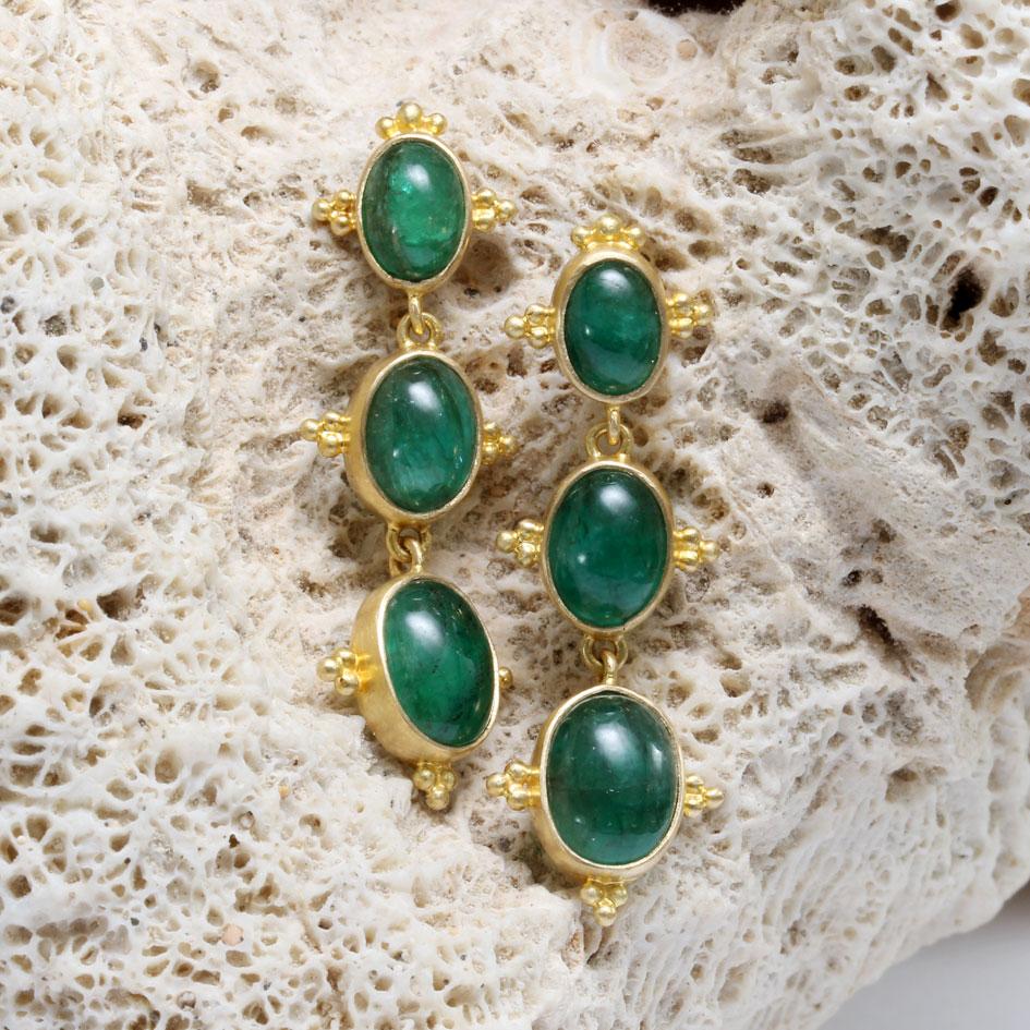 Three deep green Zambian oval cabochon emeralds are arranged in increasing sizes starting from an upper post of 5x7 mm, to 6x8 mm, to 7x9 mm.  Each stone is set in a matte-finish 18K bezel with 3 small 