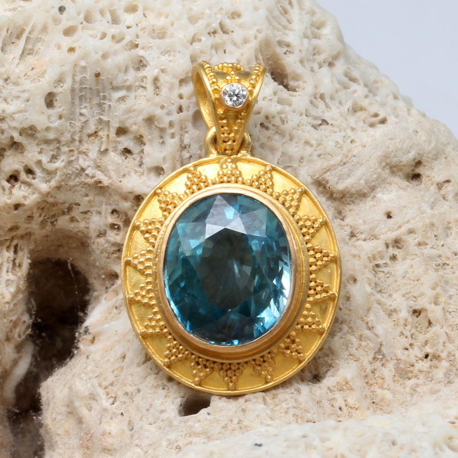 Uno zircone blu cambogiano ovale sfaccettato di 10 x 12 mm è centrato in una montatura ovale in oro di alta qualità lavorata artigianalmente con granulazione 