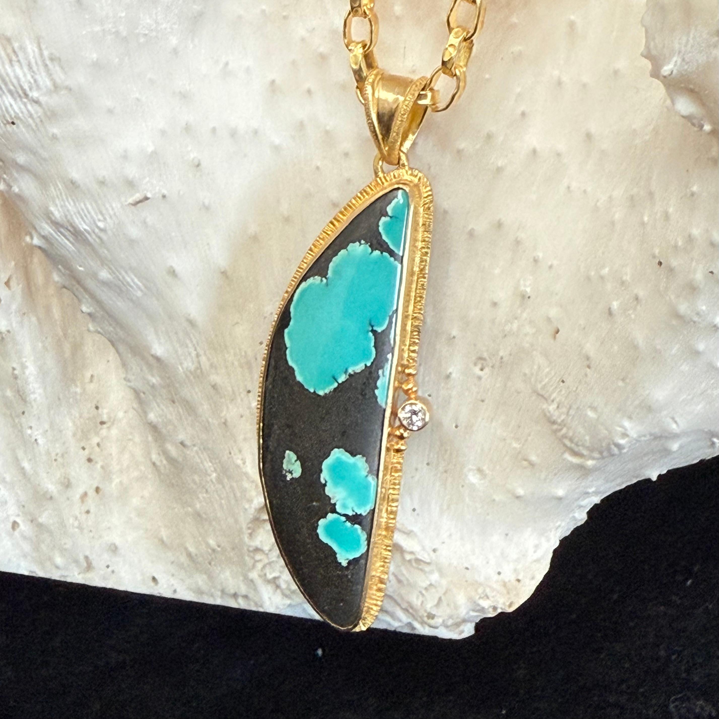 Un cabochon de 11 x 37 mm de turquoise extrêmement variée présente un incroyable motif de bleu clair et de noir dans une monture artisanale à double chaton en or 18 carats à texture linéaire. Un seul diamant VS1 de 2 mm rompt la ligne verticale de
