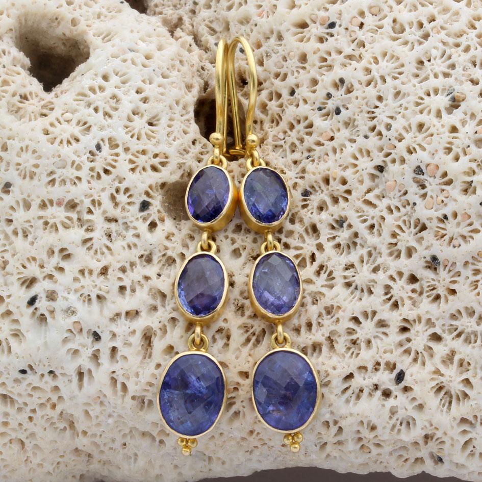 Tre tanzaniti sfaccettate a brioletta di 4 x 6 mm, 5 x 7 mm e 6 x 8 mm sono incastonate in semplici castoni in oro 18 carati con finitura opaca e sospese sotto fili di sicurezza in oro 18 carati in questa elegante creazione.  Sulla pietra più bassa