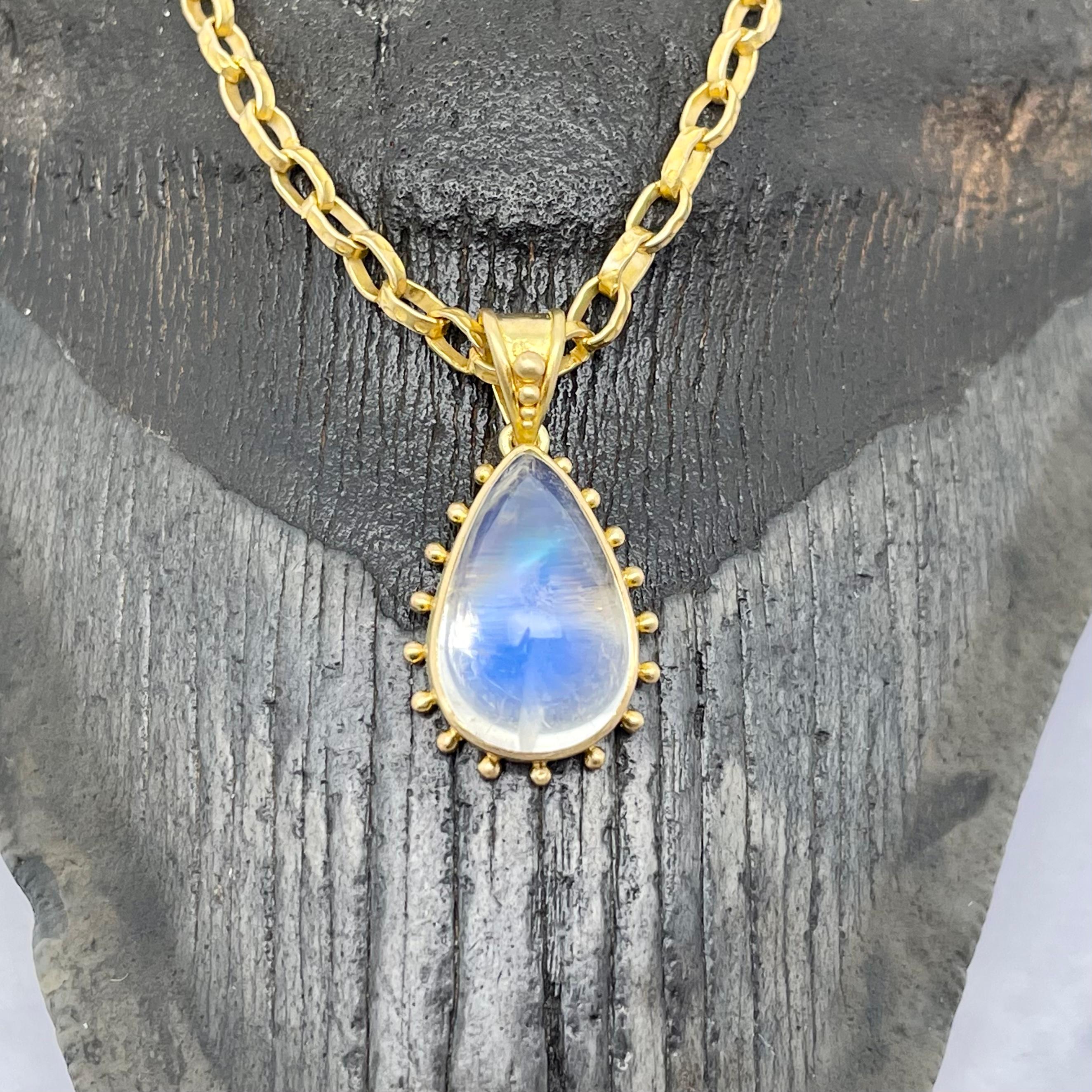 A long pear shaped 10 x 15 mm blue shimmering rainbow moonstone cabochon is set in a handmade bezel and surrounded by evenly spaced 