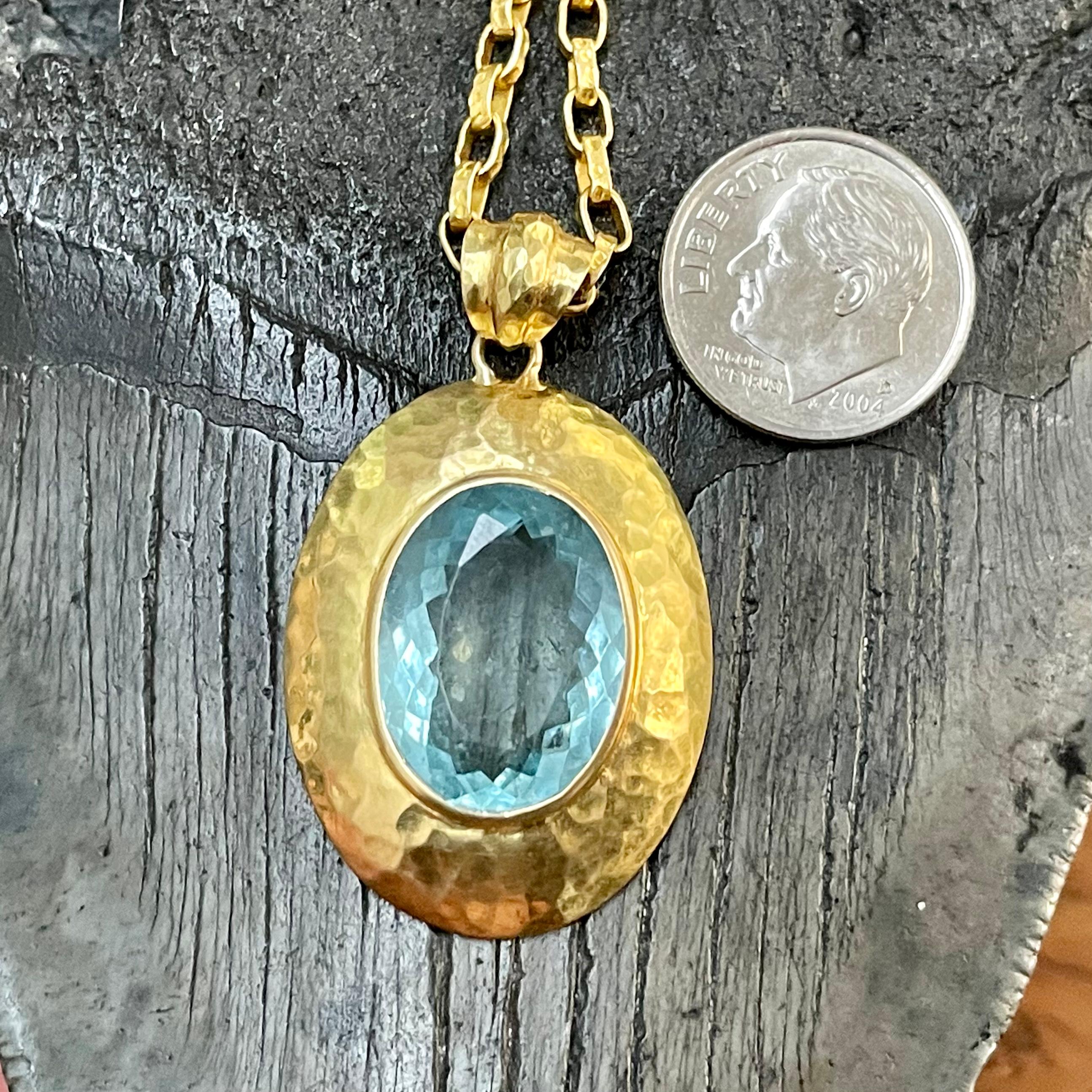 An oval 13 x 18 mm faceted aquamarine is surround in a handmade hammered oval surrounding domed setting with similar hammered bail above. A simple yet attractive complement to the stone.  The 18k handmade hammered chain shown is not included but can