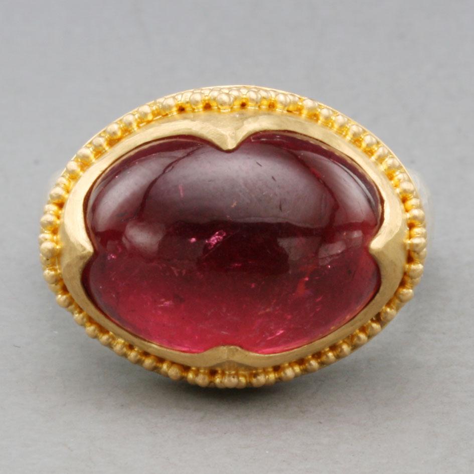Un vivace cabochon ovale di tormalina rosa, di 12 x 16 mm, è pesantemente incastonato in un'incastonatura d'ispirazione antica in oro granulato 22 carati a 4 punte con struttura martellata e finitura opaca, su un gambo affusolato in argento