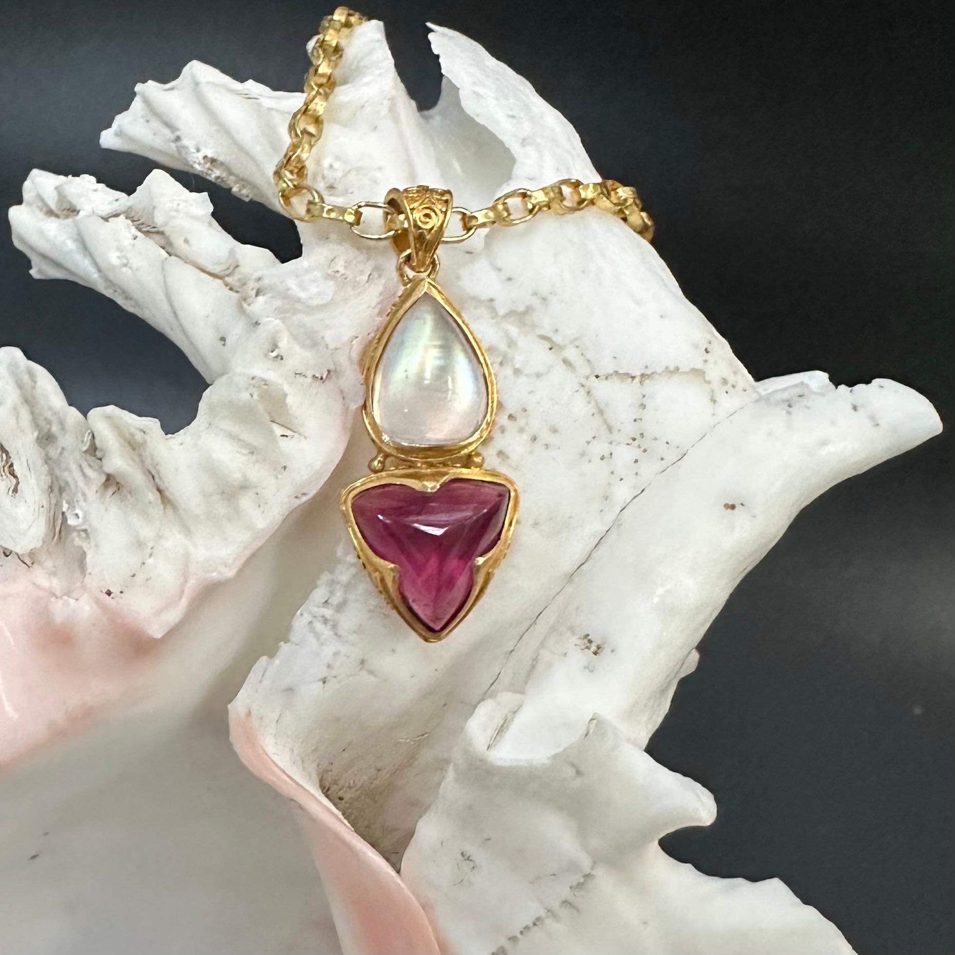 Un trillium cabochon di tormalina rosa di 11 mm è apposto sotto un vivace cabochon di pietra di luna arcobaleno a forma di pera di 9 x 11 mm in un ricco oro ad alta caratura in questo pendente ben ornato.  La pietra trillium è circondata da un