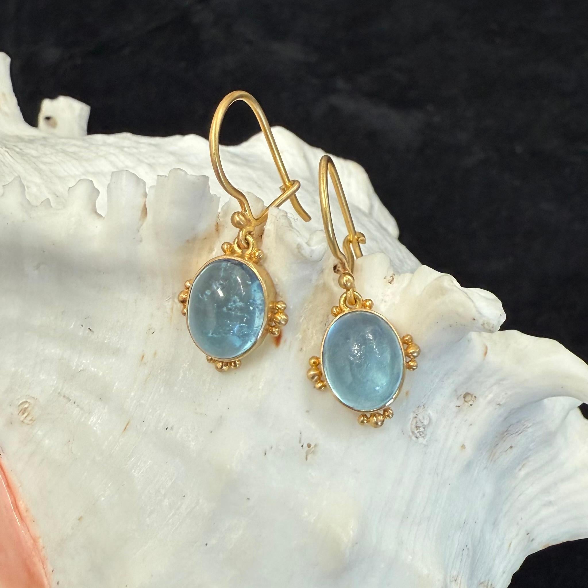 Two sea-blue 8x 10 mm oval cabochon aquamarines are set in artisan crafted 18K gold bezels with graduated 